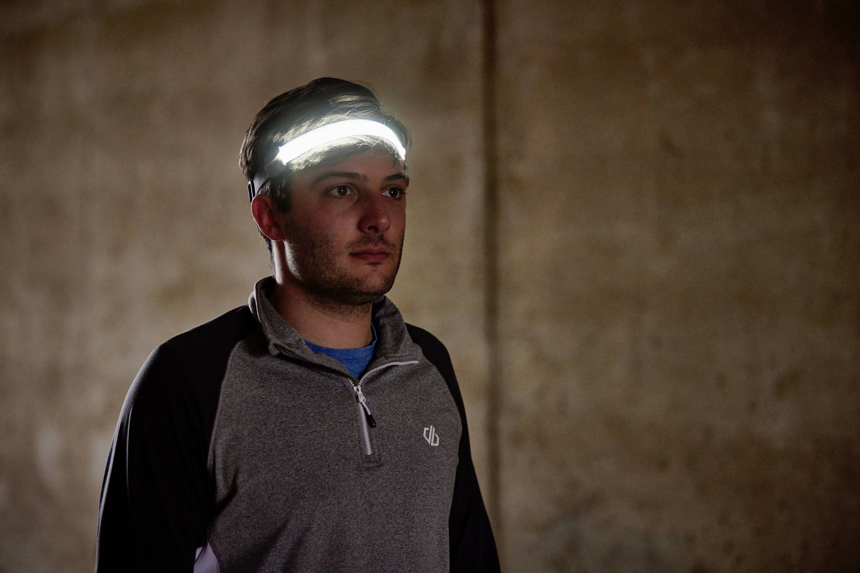 Ein Mann in Sportkleidung trägt ein leuchtendes Stirnband in einem dunklen Raum.