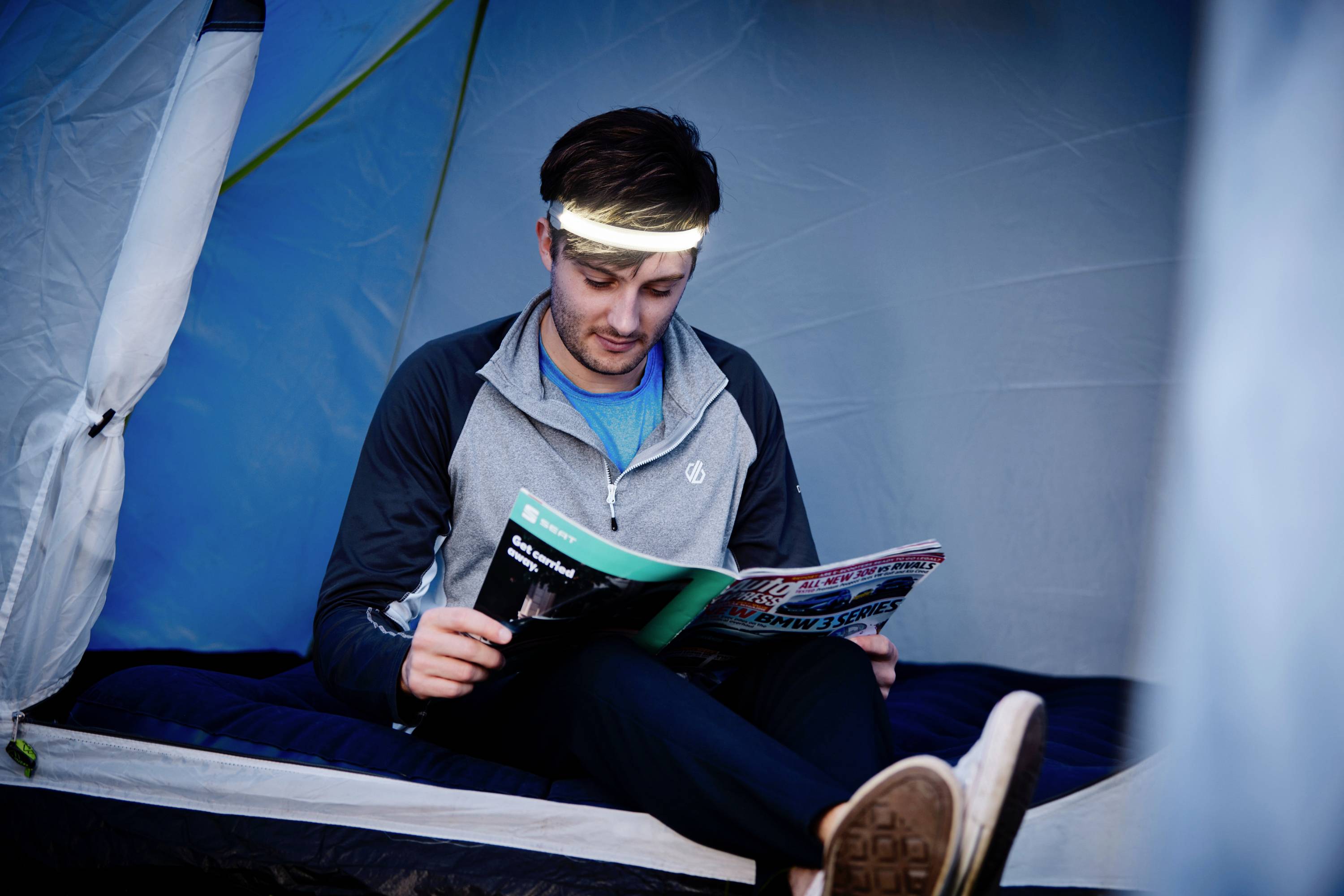 Ein Mann mit Stirnlampe liest eine Zeitschrift im Inneren eines Zeltes.