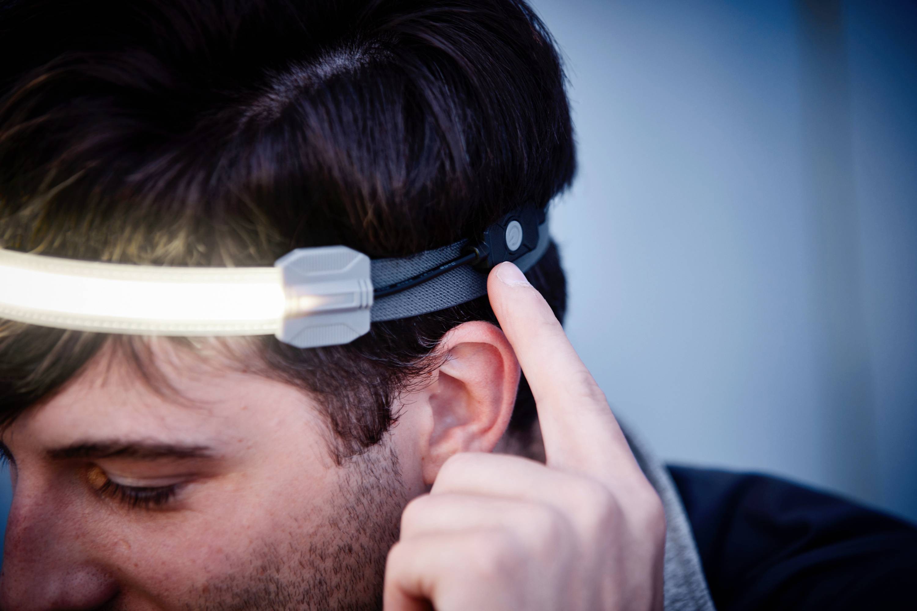 Eine Person trägt ein Stirnband mit einem integrierten Licht. Sie zeigt mit dem Finger auf den seitlichen Bedienknopf des Stirnbands.