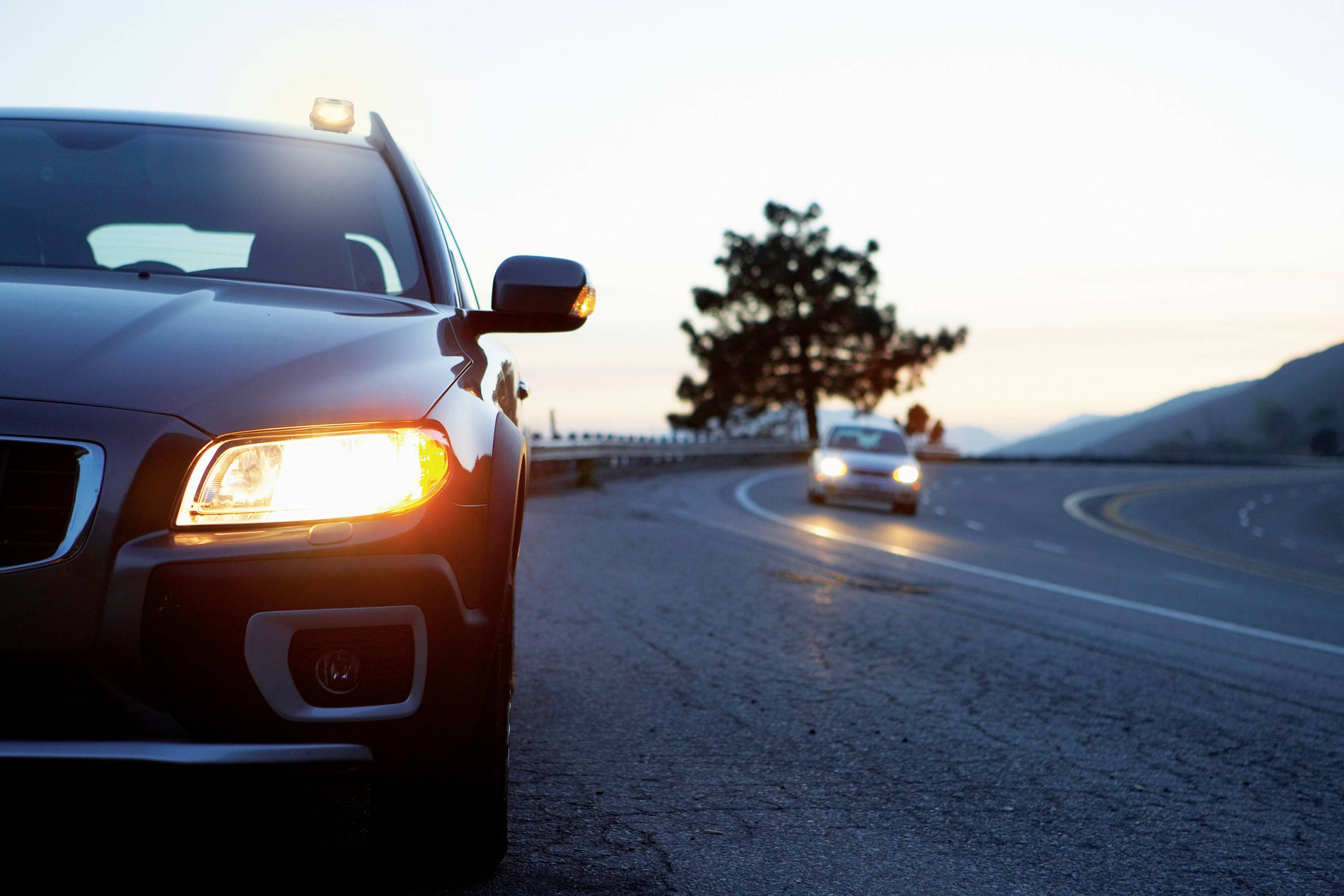 Auto auf einer Landstraße mit eingeschaltetem Scheinwerfer in der Dämmerung, weiteres Fahrzeug nähert sich von der anderen Seite.