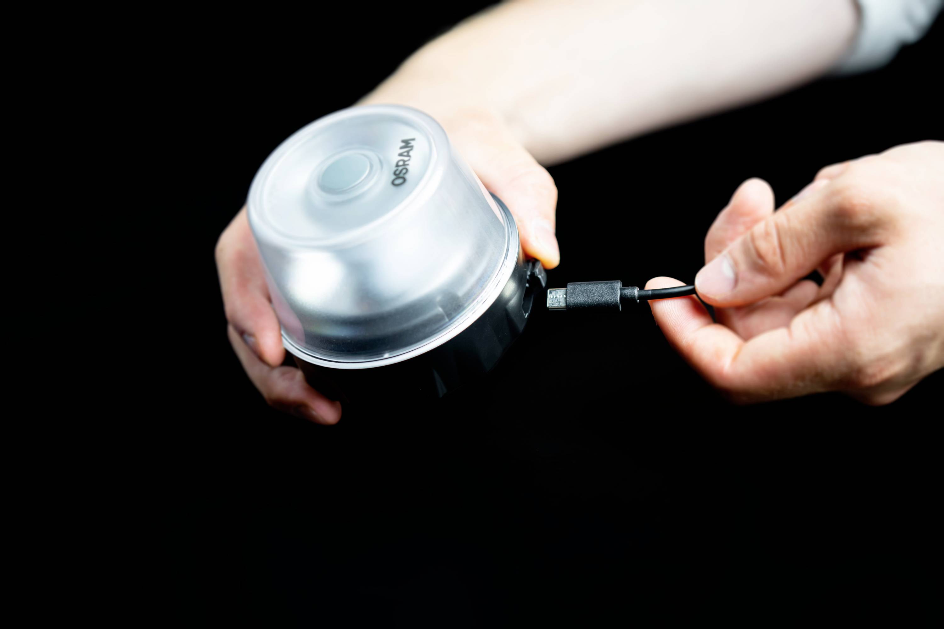 Eine Person hält ein rundes elektronisches Gerät mit einem Kabel, das an das Gerät angeschlossen wird.