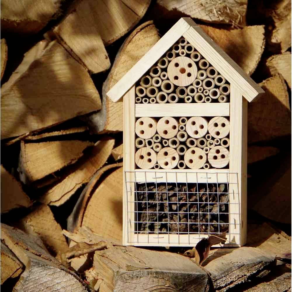 Ein Insektenhotel aus Holz mit verschiedenen Fächern und Materialien, steht vor einem Stapel geschnittener Holzscheite.