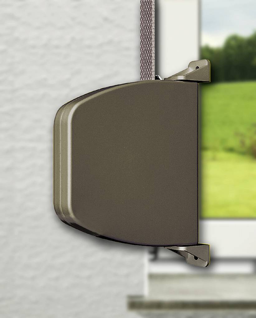 Eine braune Jalousienbefestigung an der Wand neben einem Fenster mit Blick auf grüne Wiesen.