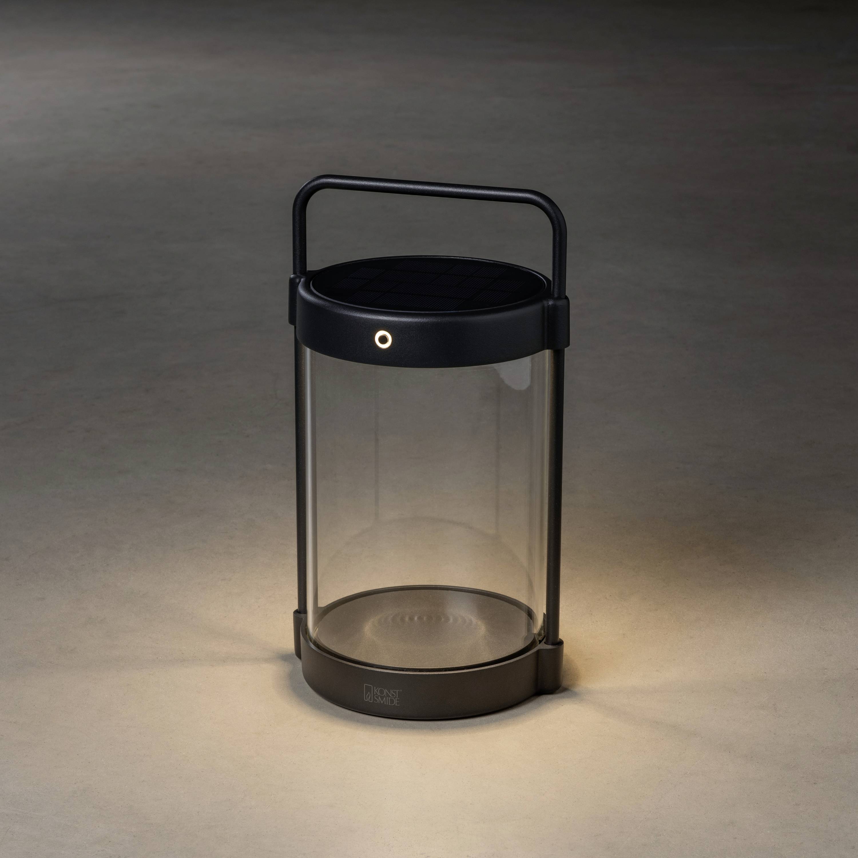 Solarlampe mit schwarzem Metallrahmen und Glaszylinder, im Dunkeln leuchtend. Ideal für umweltfreundliche Außenbeleuchtung.