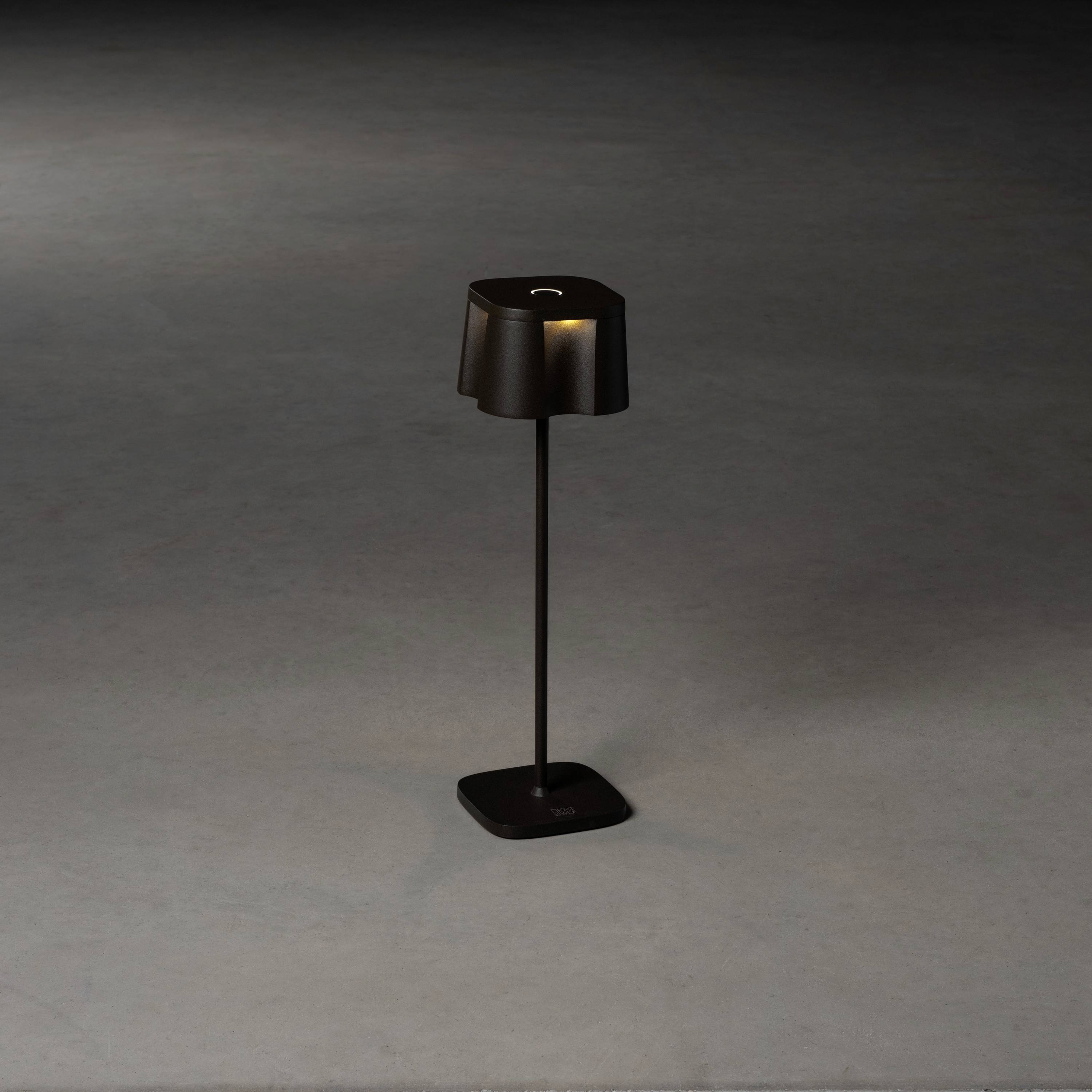Eine schwarze, moderne Stehlampe mit quadratischem Lampenschirm steht auf einem grauen Boden, beleuchtet sanft die Umgebung.