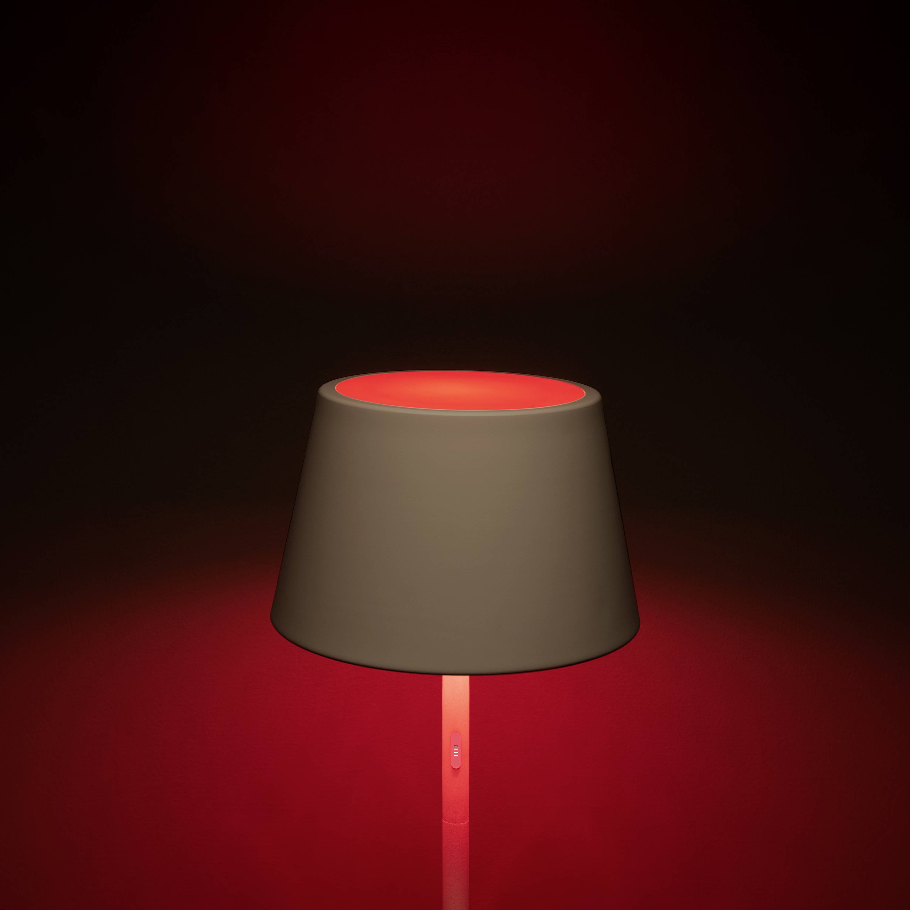 Eine Tischlampe mit rotem Licht auf dunklem Hintergrund. Die Lampe ist zentral platziert und leuchtet intensiv.