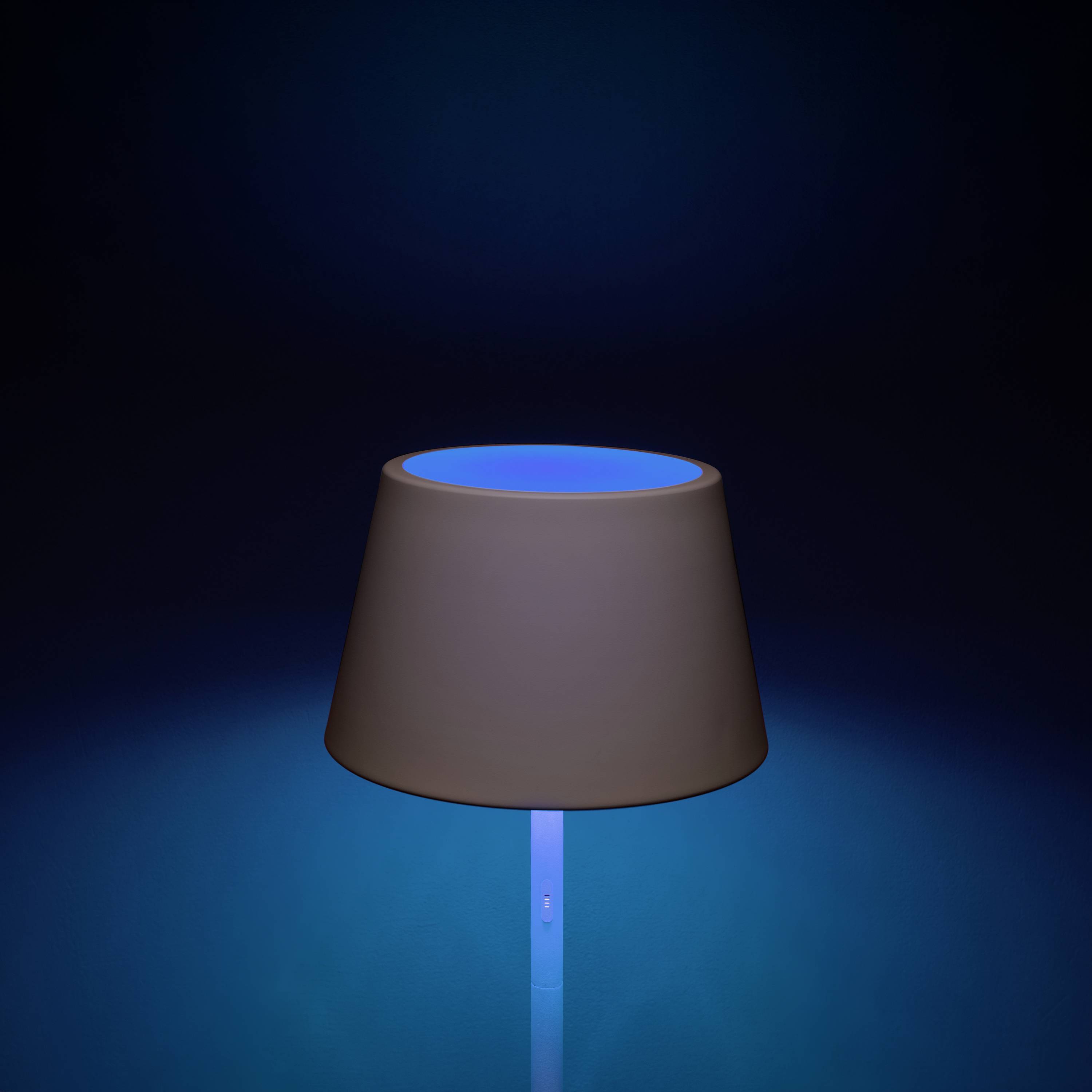Eine Tischlampe mit blauem Leuchten strahlt in einem dunklen Raum.