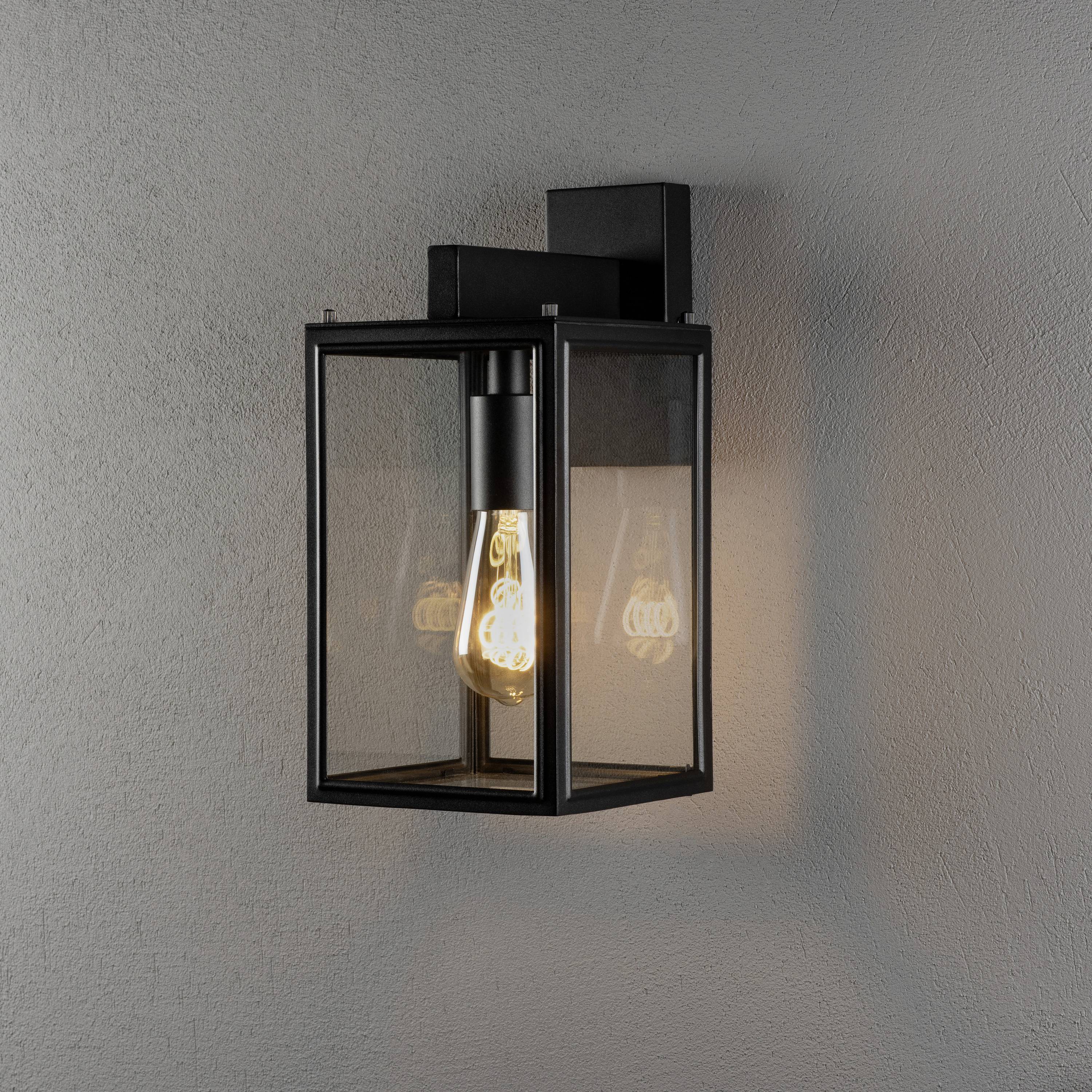 Schwarze Wandlaterne mit sichtbarer Glühbirne, in modernem Design, beleuchtet graue Wand subtil.