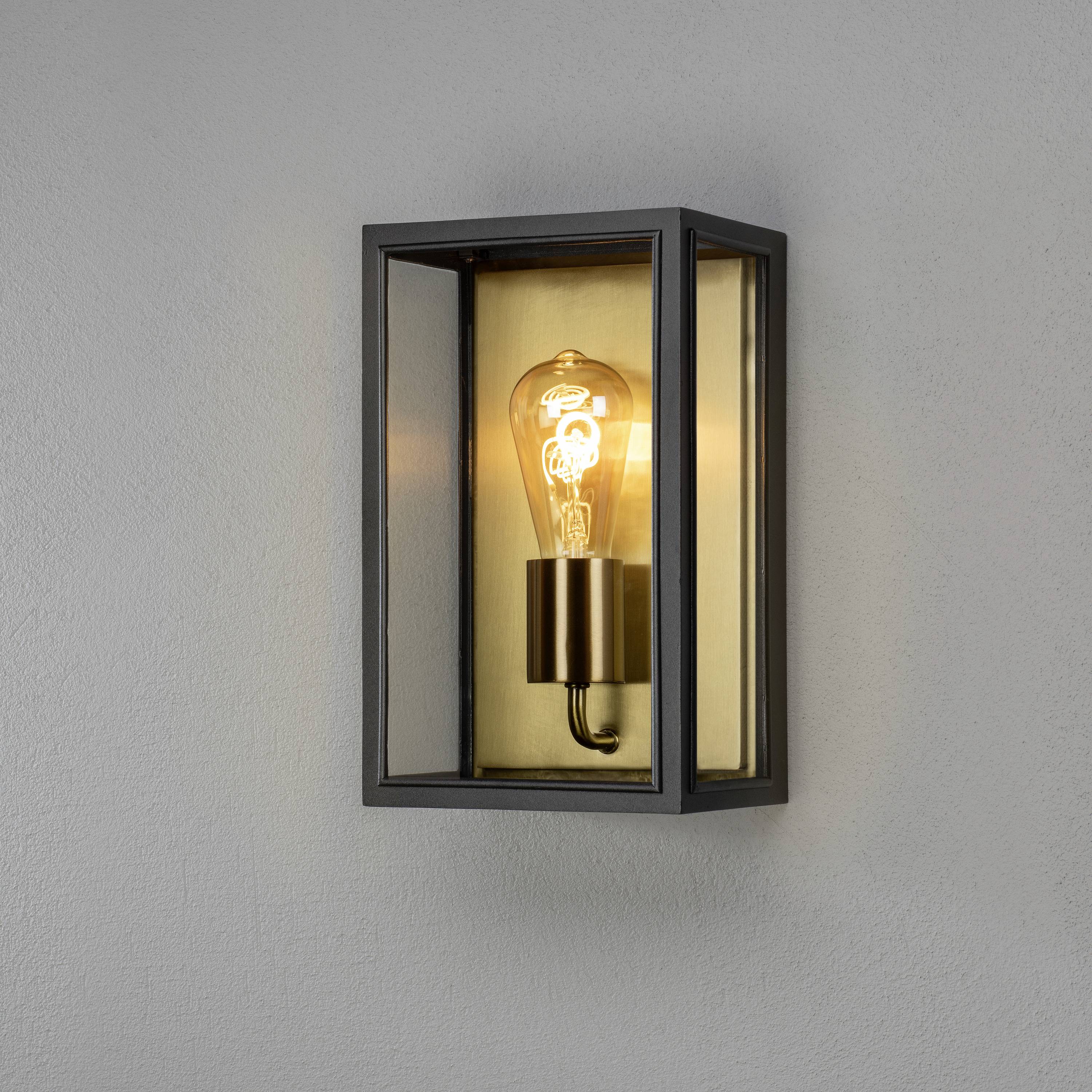 Wandleuchte mit Glühbirne in rechteckigem Metallrahmen, die warmes Licht abstrahlt.