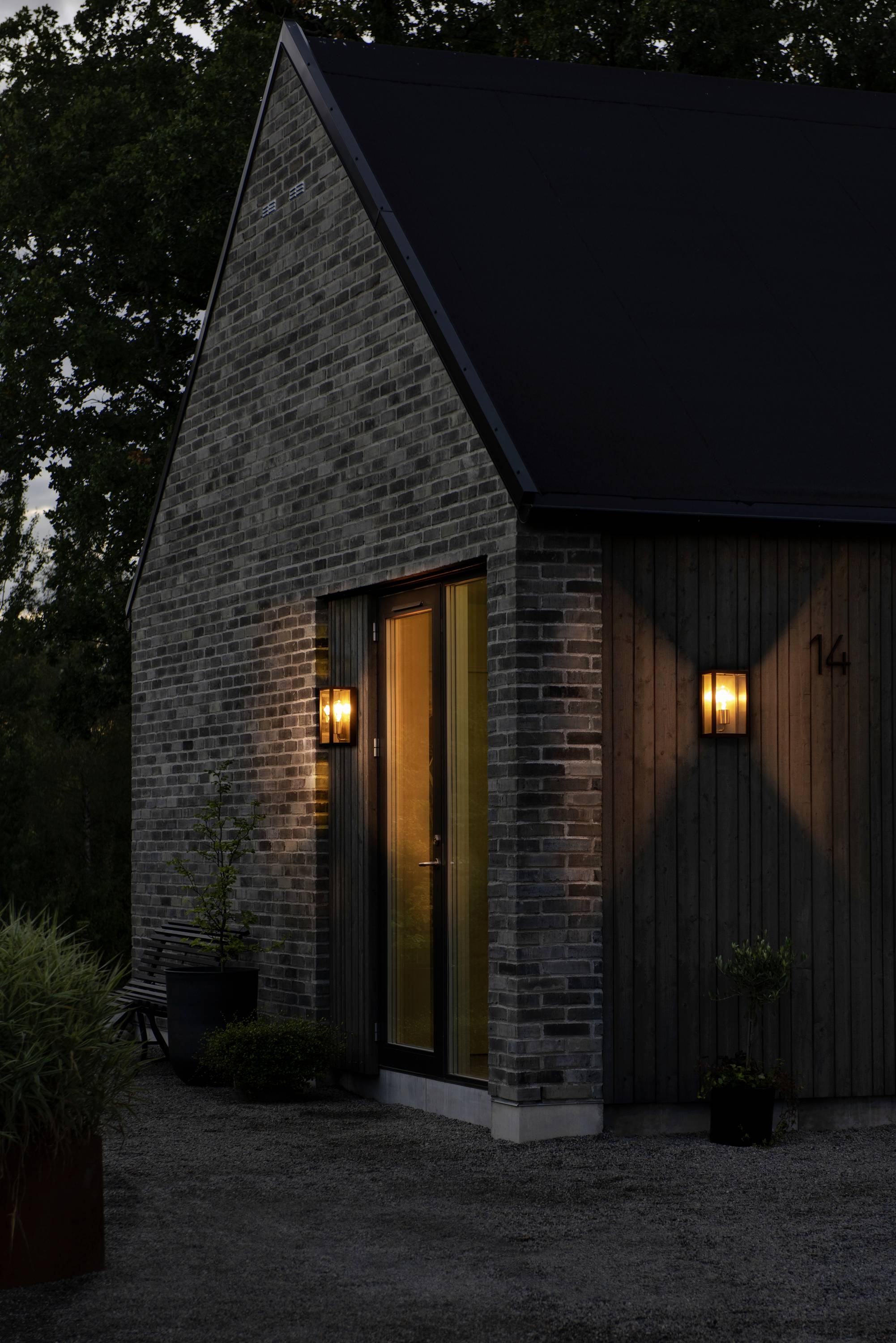 Licht beleuchtetes modernes Haus mit Ziegelmauerwerk und Seitenbeleuchtung bei Dämmerung. Tür spiegelt warmes Licht.