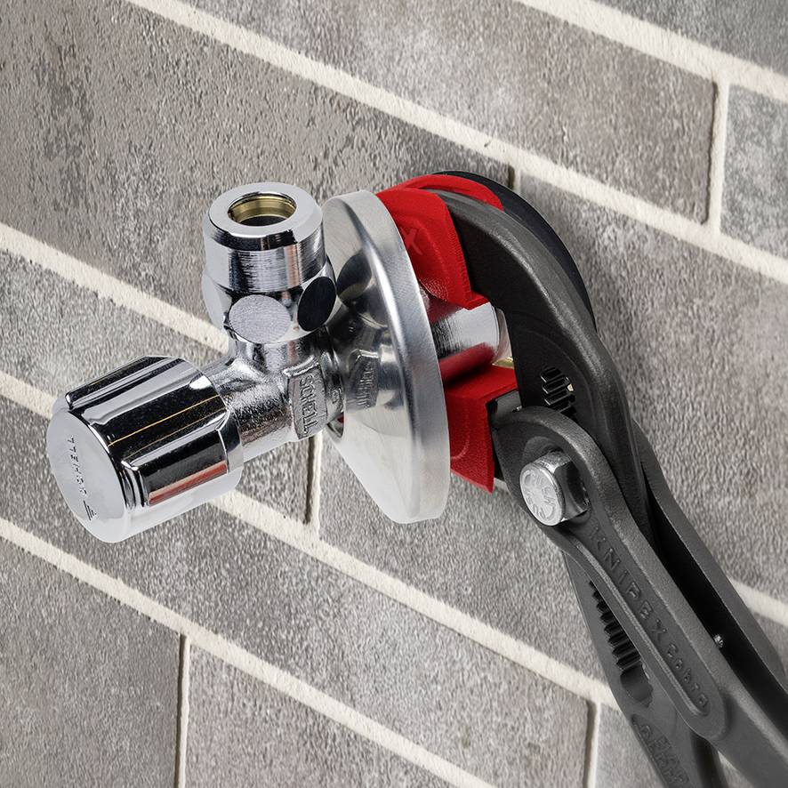 Zange dreht an einem silbernen Wasserhahnventil, das an einer grauen gefliesten Wand befestigt ist.