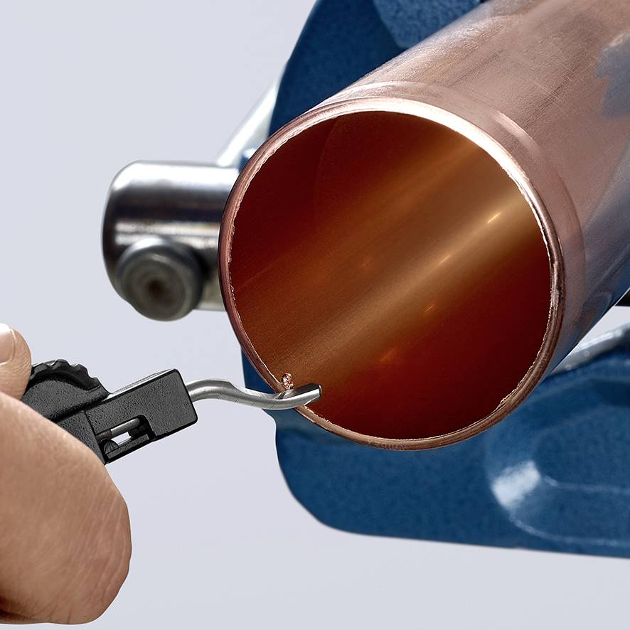 Hand, die ein Rohrentgrater-Werkzeug an einem Kupferrohr verwendet. Das Werkzeug entfernt scharfe Kanten, um eine glatte Oberfläche zu schaffen.