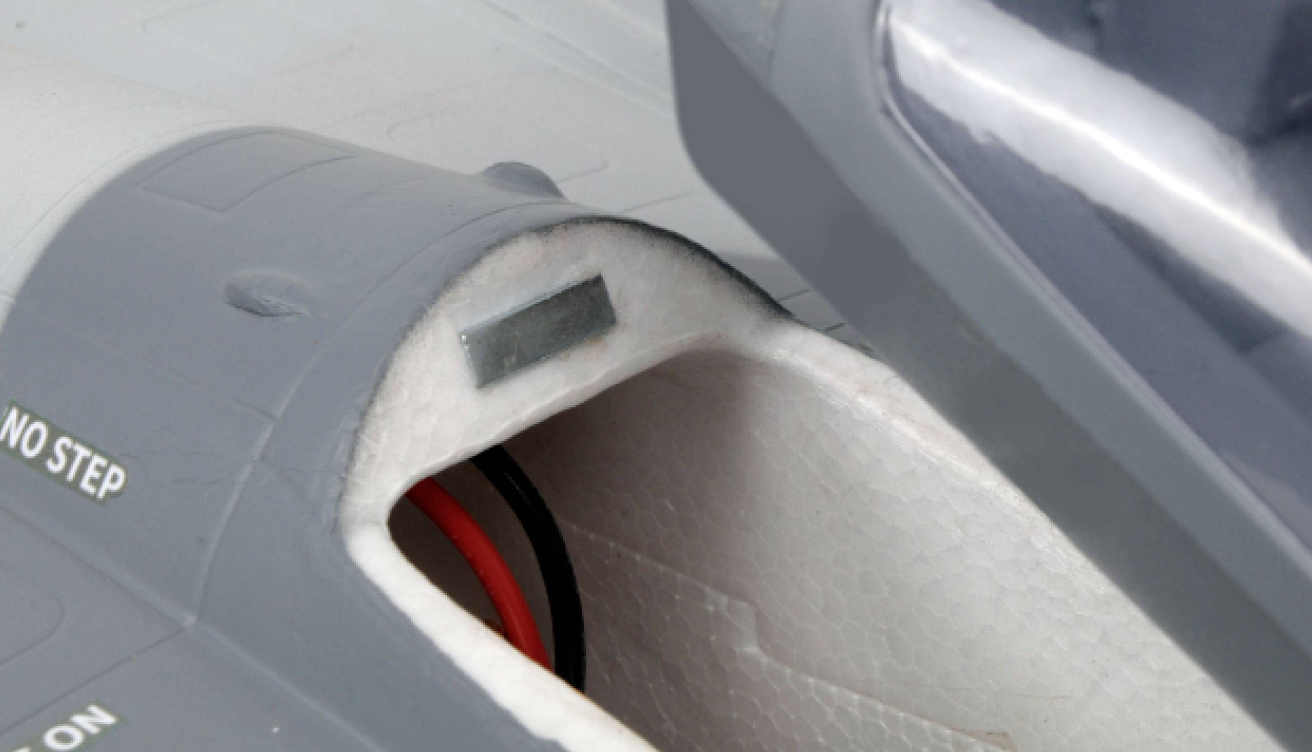 Nahaufnahme eines Modellflugzeug-Cockpits mit geöffnetem Cockpitsitz. Kabel und Text 'NO STEP' auf dem grauen Flugzeug dargestellt.