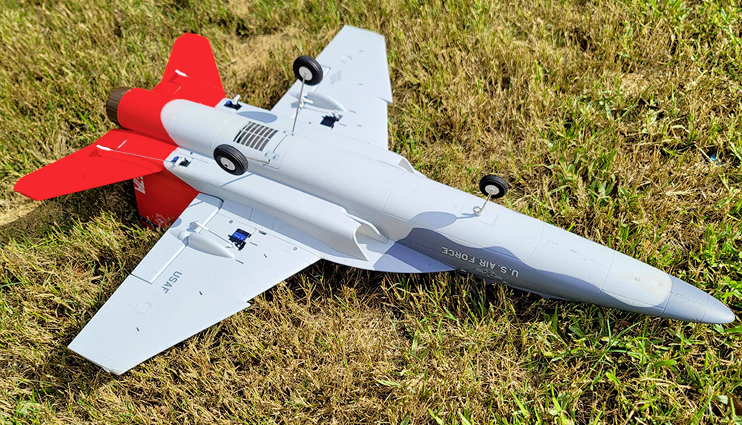 Ein Modellflugzeug mit roten Heckflügeln liegt auf einem Grasfeld. Auf dem Rumpf steht 'U.S. Air Force'.