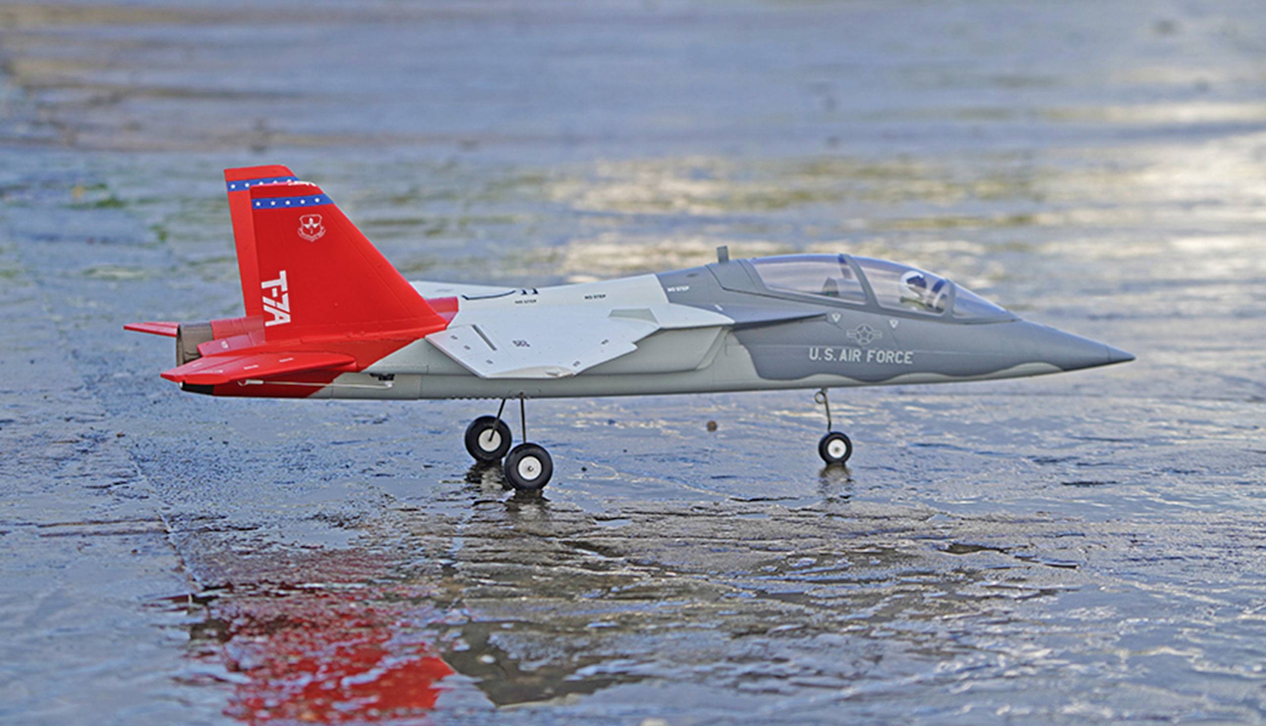 Ein Modellflugzeug der US Air Force steht auf nassem Boden. Es hat einen grauen Rumpf und rote Heckflügel.