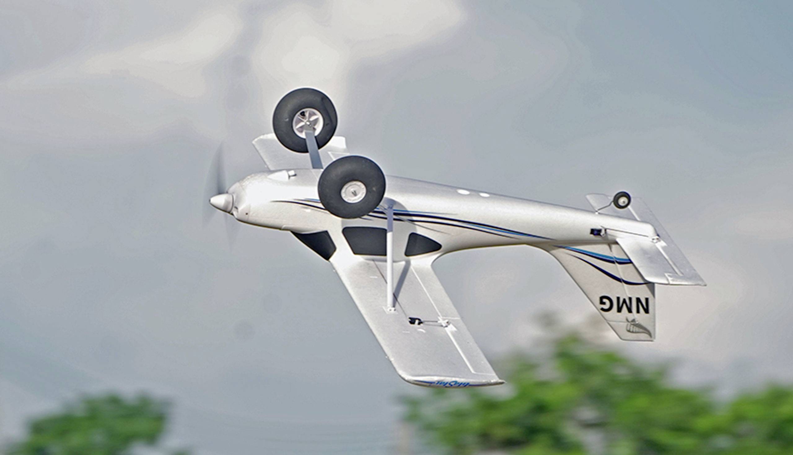 Ein ferngesteuertes Modellflugzeug fliegt kopfüber am Himmel. Sichtbar sind Details der Flügel, Fahrwerk und Propeller.