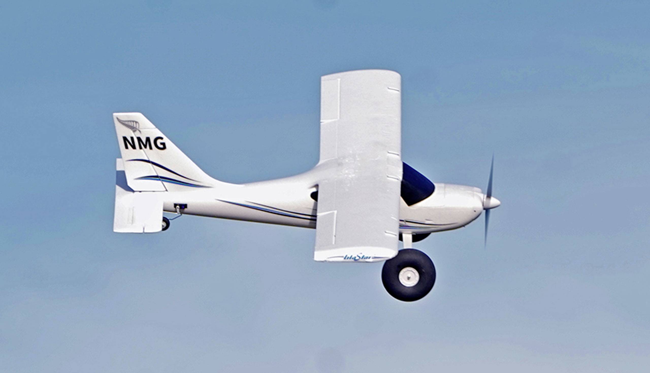 Ein kleines einmotoriges Flugzeug fliegt bei klarem Himmel. Es ist weiß mit blauen Akzenten und hat das Kennzeichen 'NMG'.