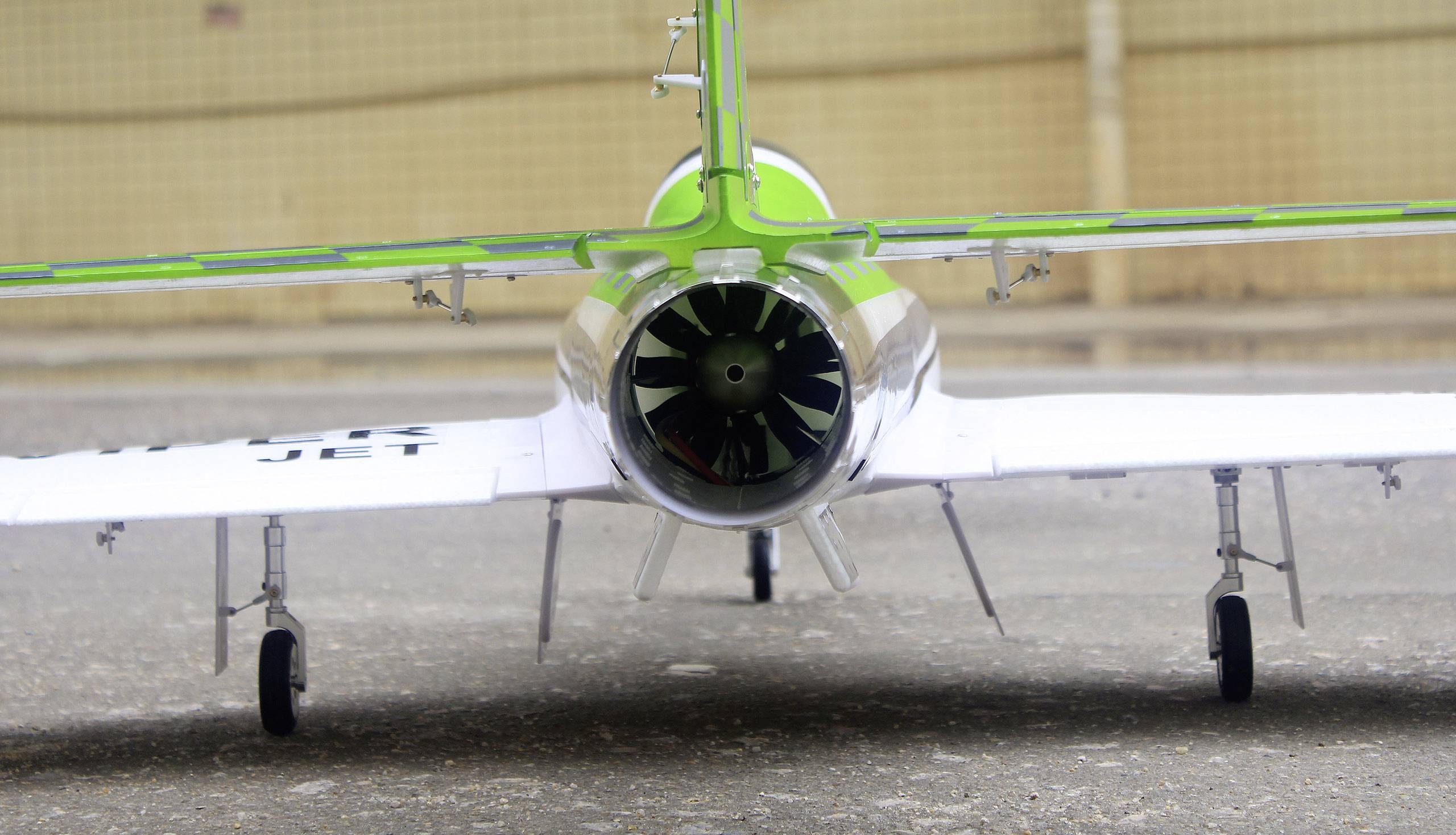 Ein kleines Modellflugzeug mit grüner und weißer Lackierung steht auf einem Asphaltboden. Man sieht den Propeller im Heck.