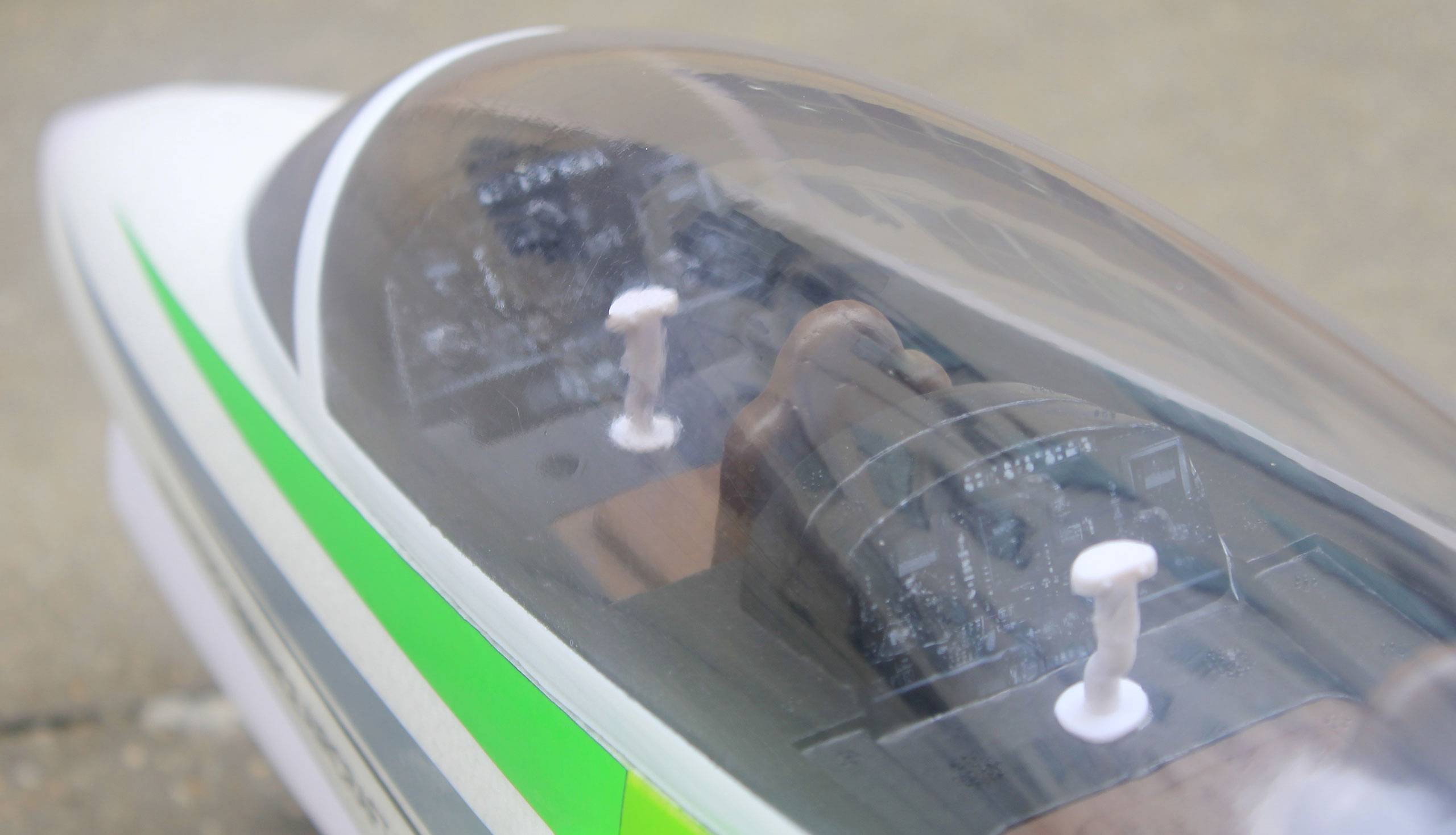 Modellflugzeug-Cockpit mit zwei Sitzen und Steuerknüppeln, durch eine durchsichtige Abdeckung sichtbar, auf einer grauen Oberfläche.