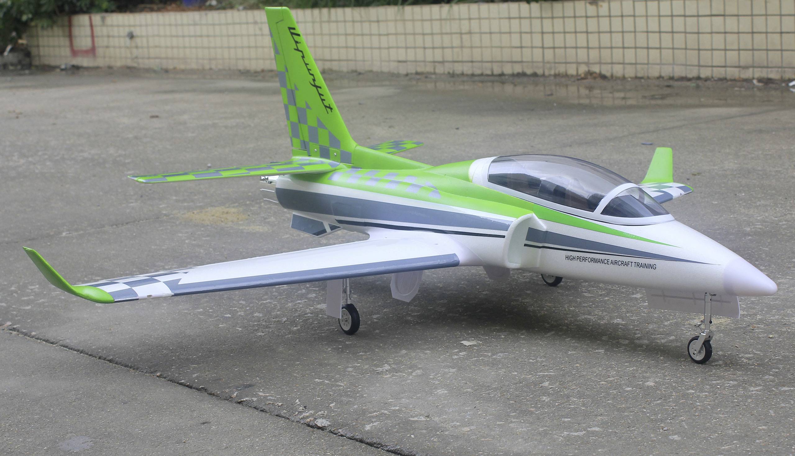 Ein Modellflugzeug in hellgrüner und weißer Lackierung steht auf einer Betonfläche. Es hat ein einziehbares Fahrwerk und einen aerodynamischen Rumpf.