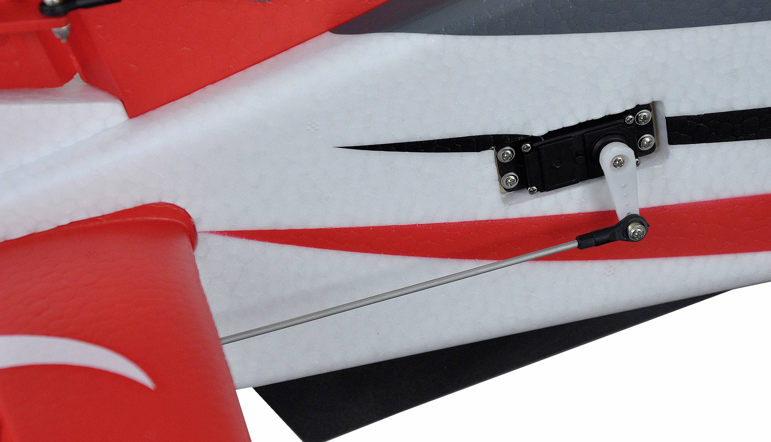 Nahaufnahme eines Modellflugzeugs mit roten und weißen Farben. Ein Steuerungsmechanismus mit Servo und Gestänge ist sichtbar.
