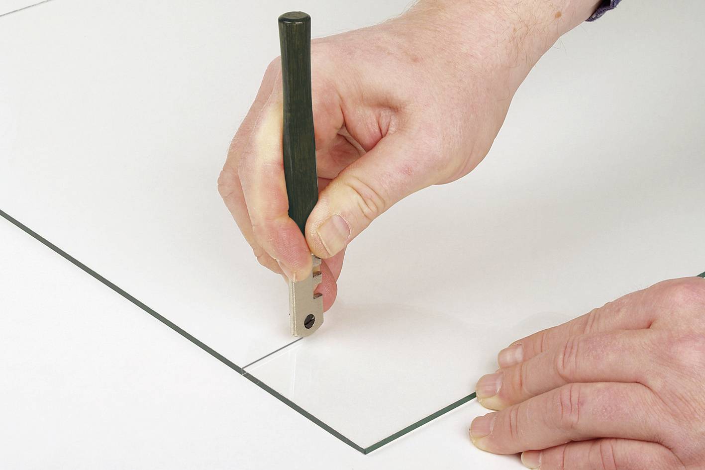 Eine Hand hält einen Glasschneider und schneidet eine gerade Linie in eine Glasscheibe.