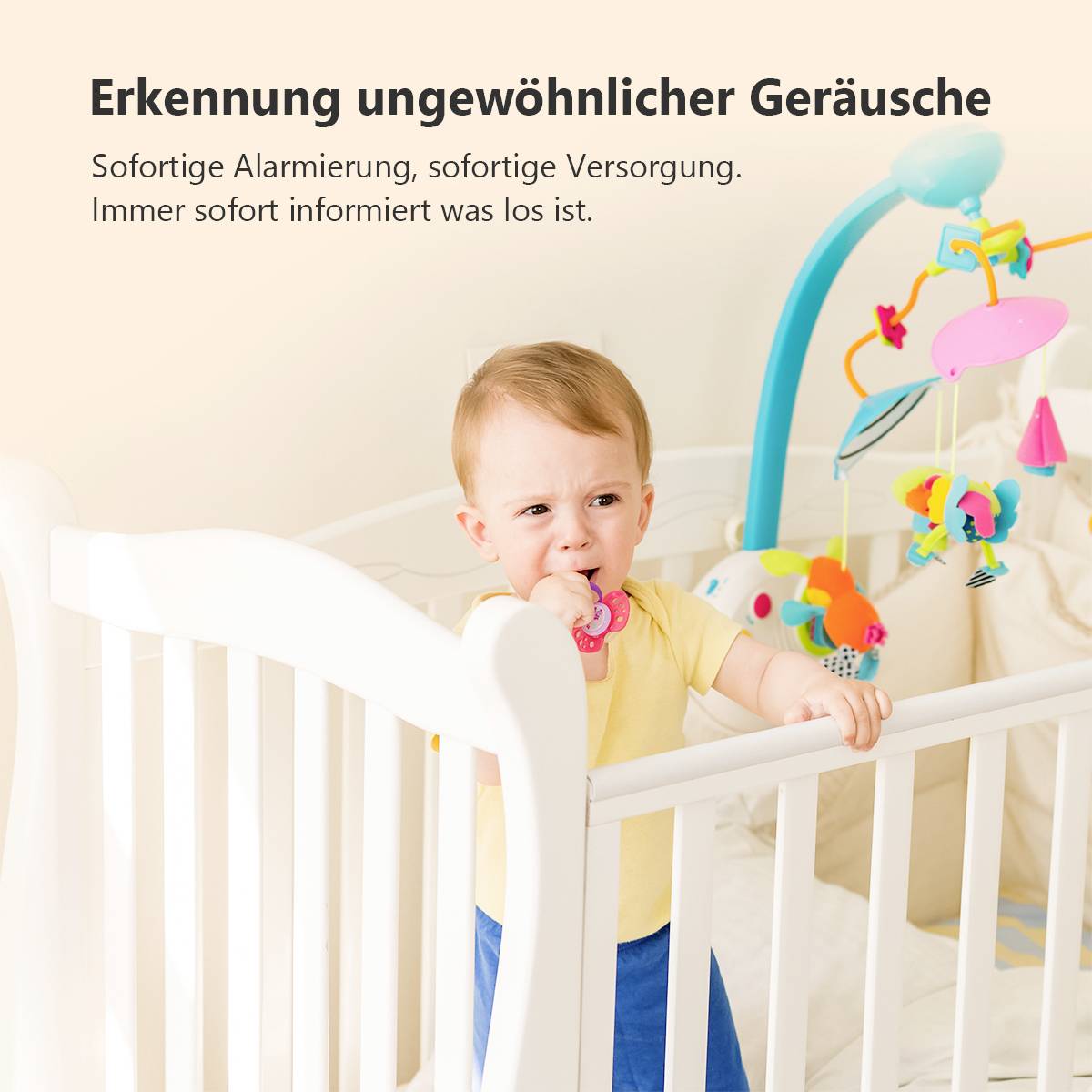 Kleinkind steht im Gitterbett, hält einen Schnuller. Text oben: 'Erkennung ungewöhnlicher Geräusche'. Spielbogen im Hintergrund.