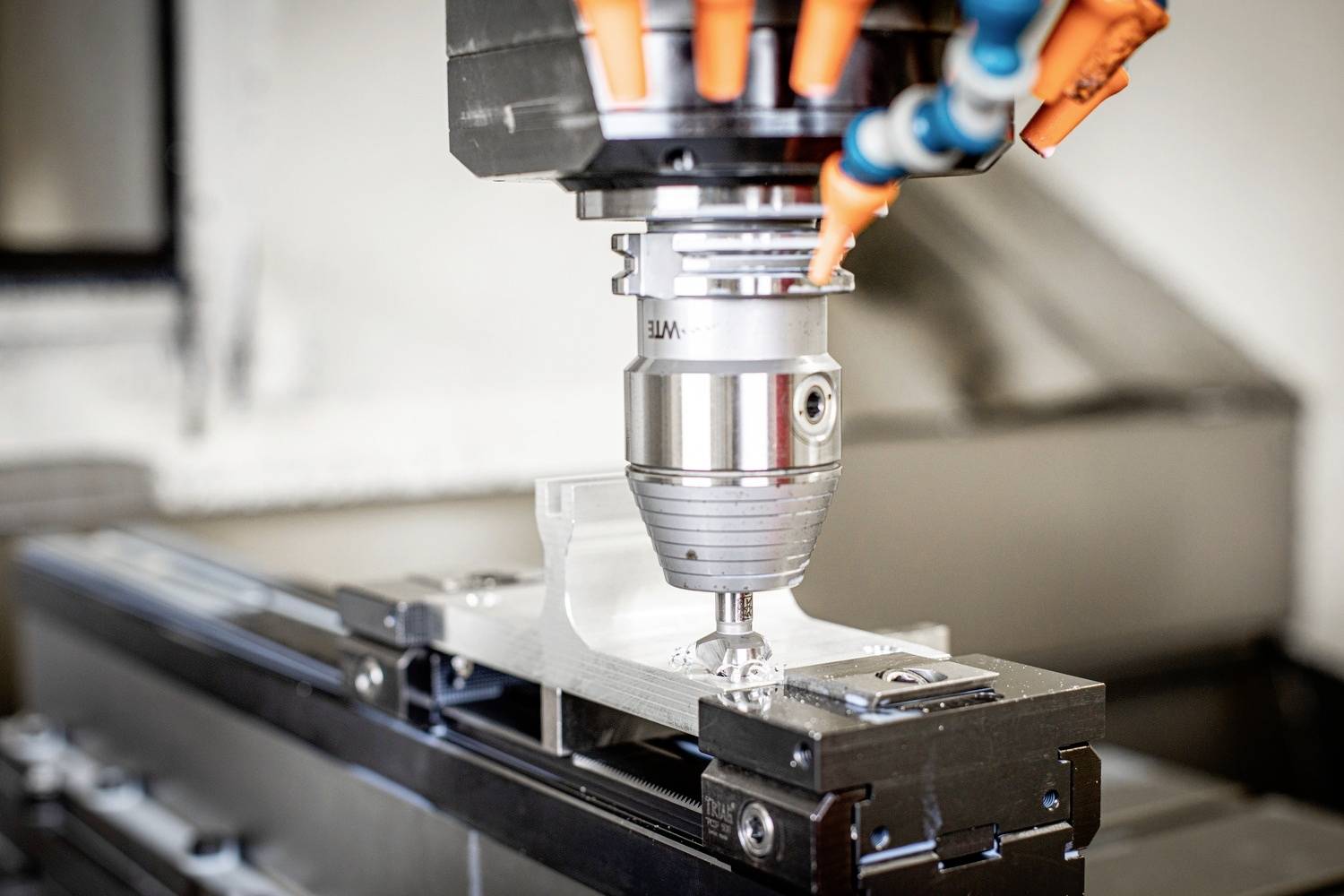 Eine CNC-Maschine bohrt präzise in ein Metallwerkstück. Orange Kabel sind über dem Bohrkopf sichtbar.