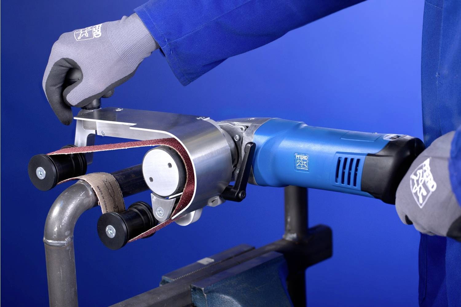 Eine Person benutzt ein elektrisches Schleifwerkzeug, um ein Metallrohr zu bearbeiten. Das Werkzeug ist blau und wird mit Handschuhen gehalten.