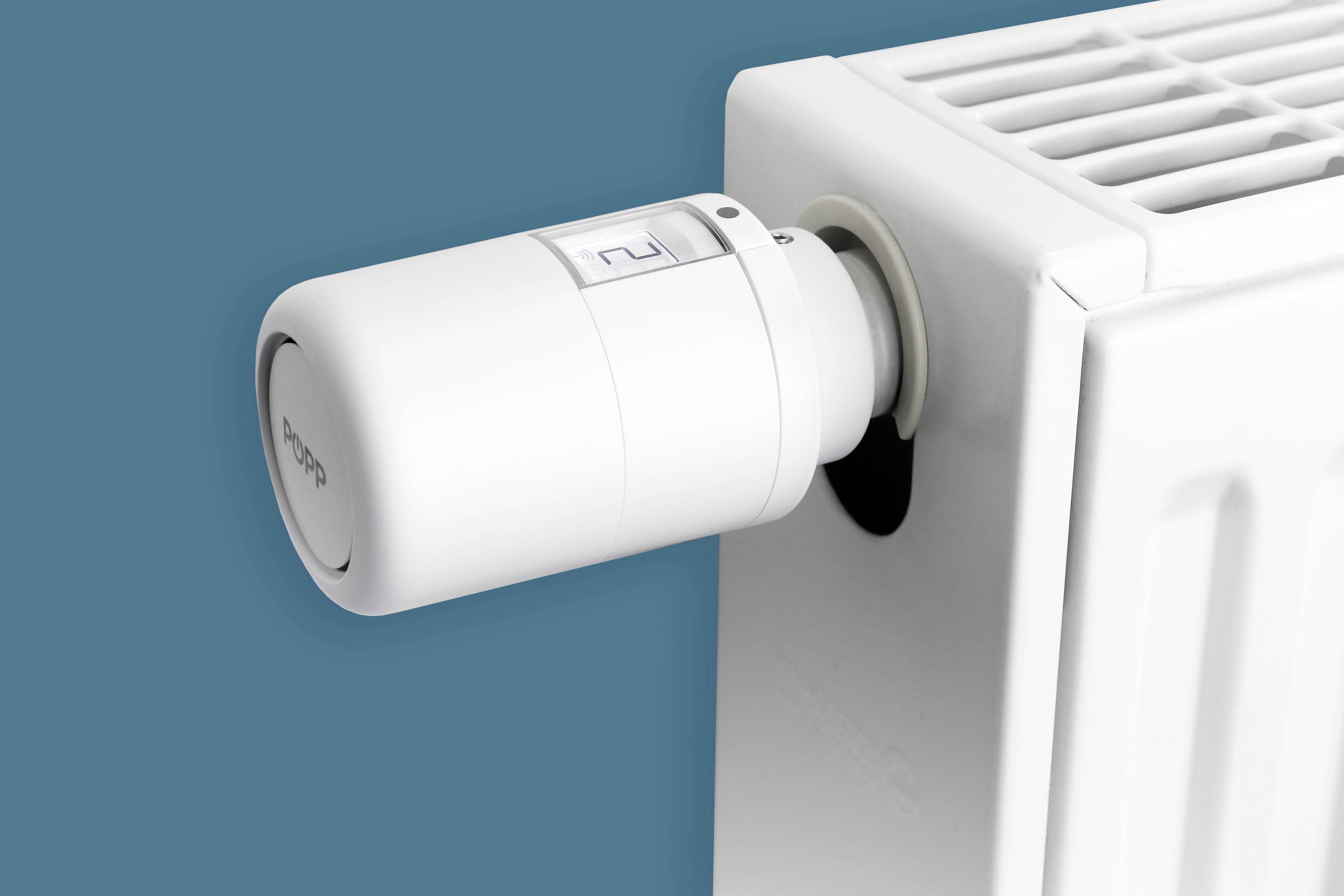 Heizkörper mit einem weißen, modernen Thermostatregler vor blauem Hintergrund. Das Thermostat zeigt die Einstellung '2'.