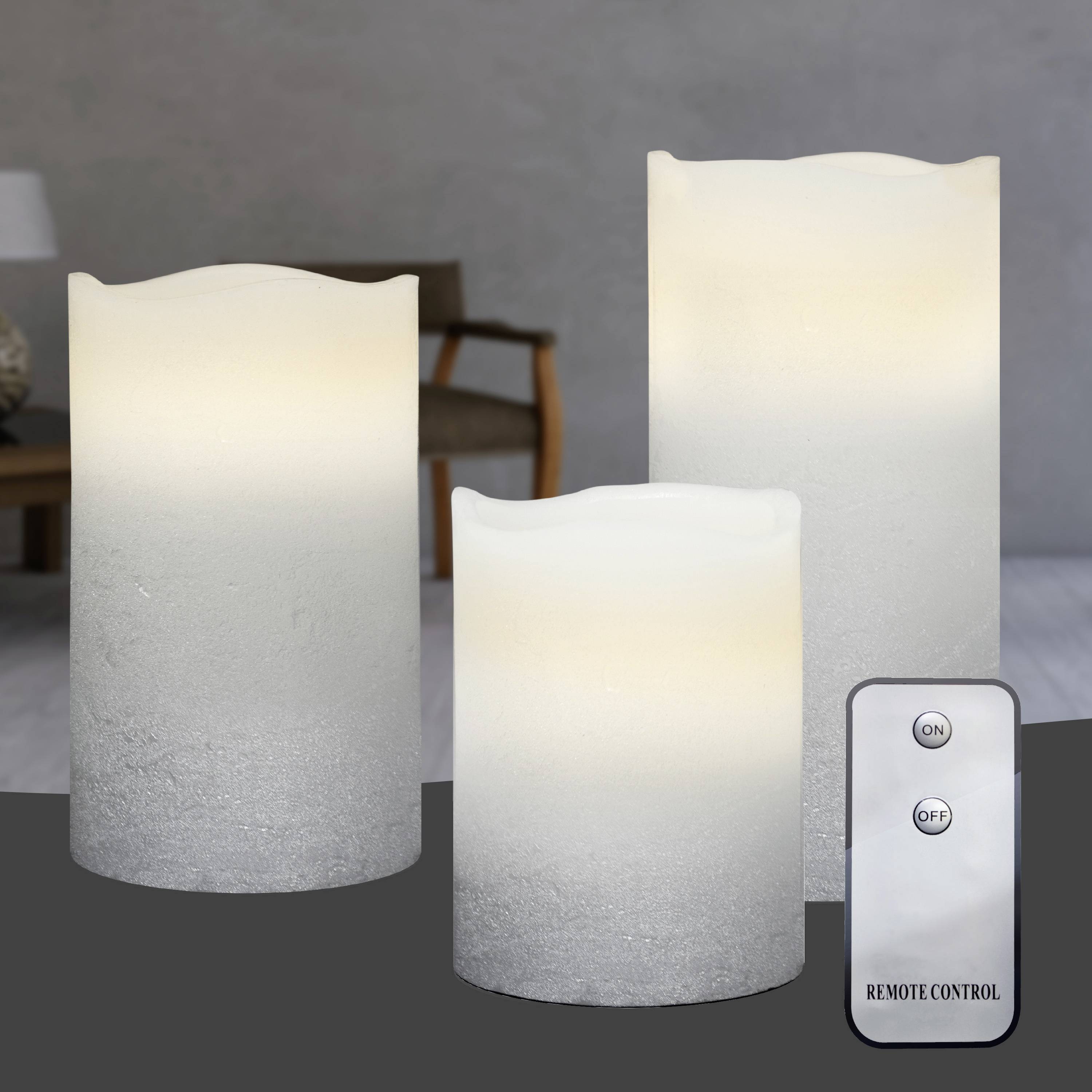 Drei elektronische Kerzen in verschiedenen Größen leuchten auf einem Tisch. Rechts unten ist eine Fernbedienung mit 'ON' und 'OFF'-Tasten. Im Hintergrund steht ein Stuhl.