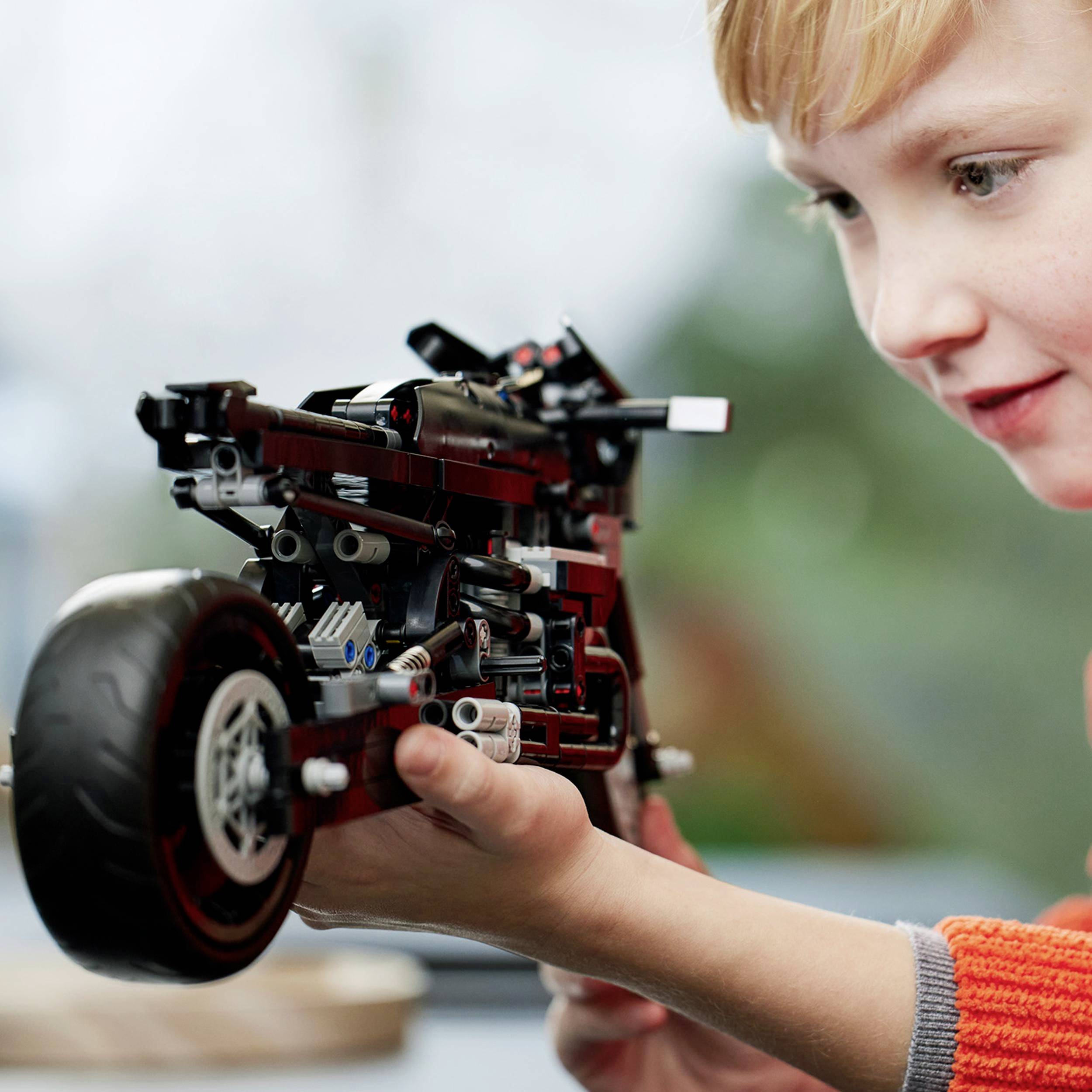 Ein Kind hält ein detailliertes, selbstgebautes Modell eines Motorrads aus Lego-Steinen. Das Kind blickt aufmerksam auf das Modell.