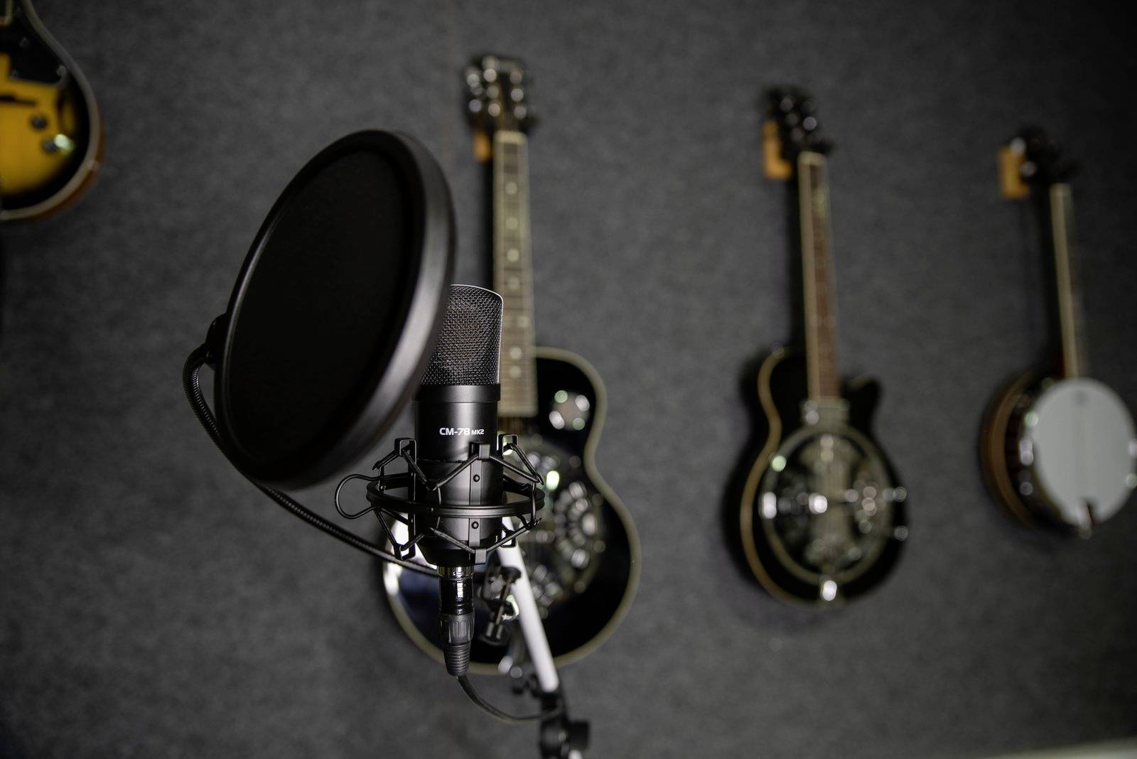 Mikrofon im Vordergrund mit mehreren Gitarren an der Wand im Hintergrund, betont Musikproduktion oder Aufnahmeumgebung.