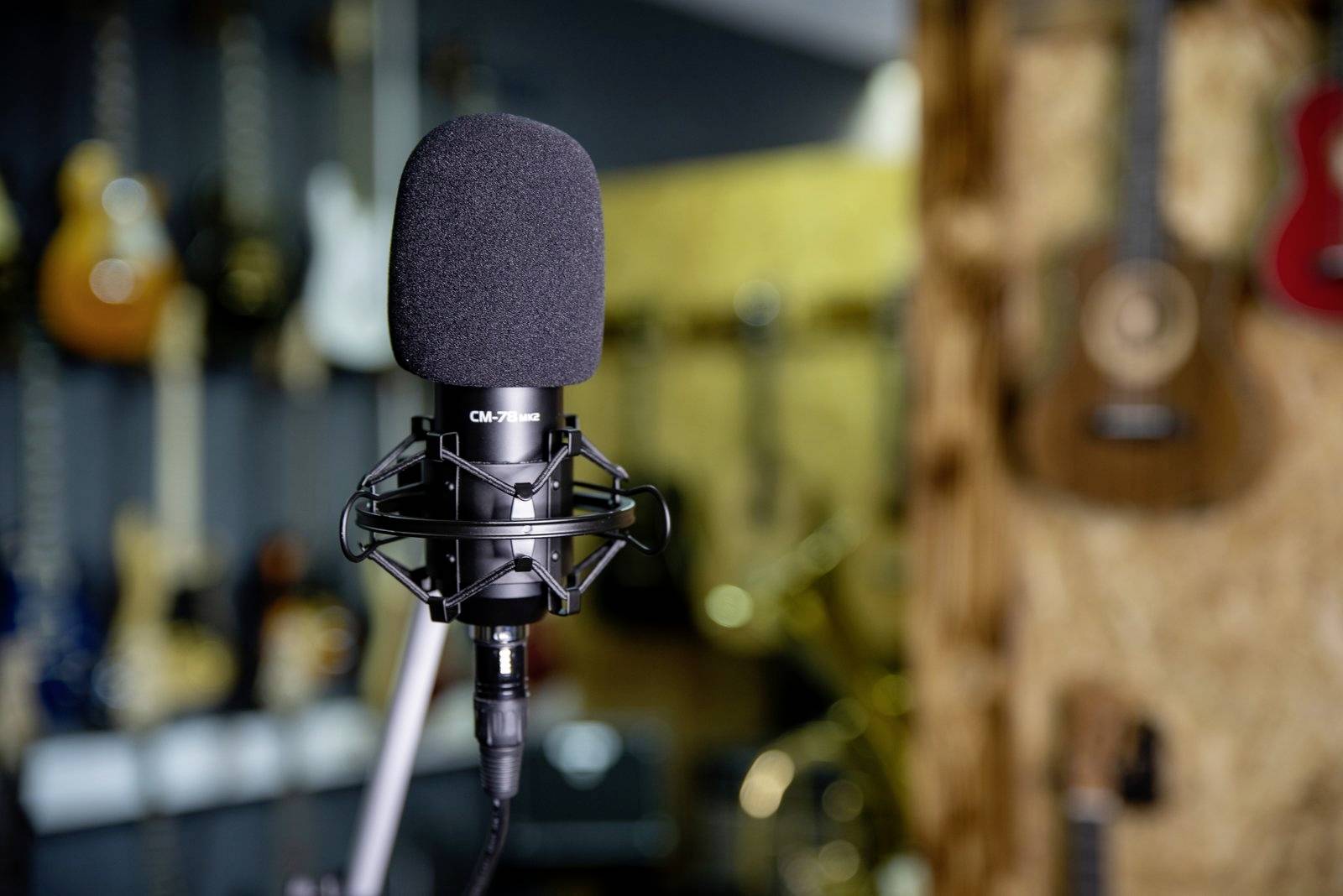Ein Mikrofon steht im Vordergrund, umgeben von unscharfen Gitarren im Hintergrund. Die Szene erinnert an ein Musikstudio.