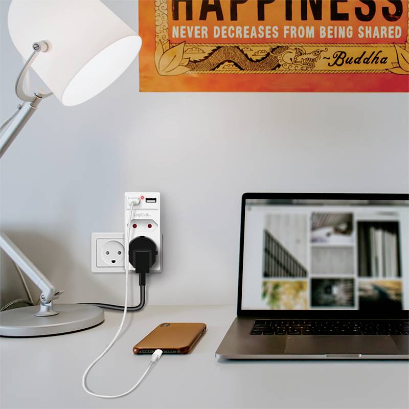 Ein Schreibtisch mit Lampe, Steckdose mit Ladekabel und einem Smartphone. Im Hintergrund ein Laptop mit geöffneter Bild-Website.
