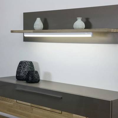 Moderne Wandbeleuchtung über einem schwebenden Regal mit zwei blauen Vasen. Darunter befindet sich ein Sideboard mit zwei schwarzen Gitterdekorationen.