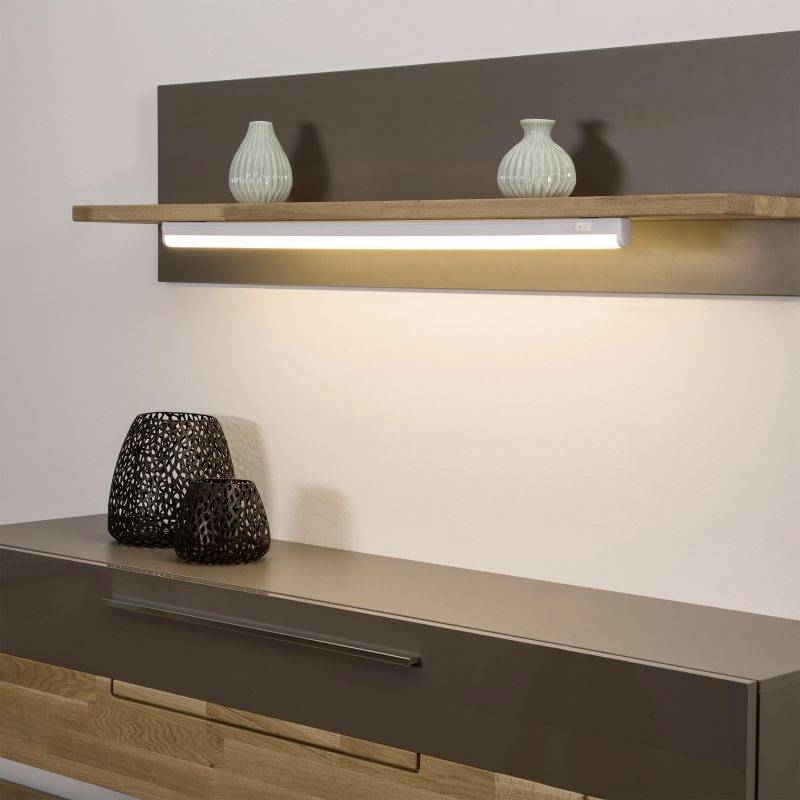 Ein modernes Sideboard mit einer Holzleiste darüber, die zwei türkisfarbene Vasen und eine beleuchtete Lampe trägt. Daneben schwarze Körbe.