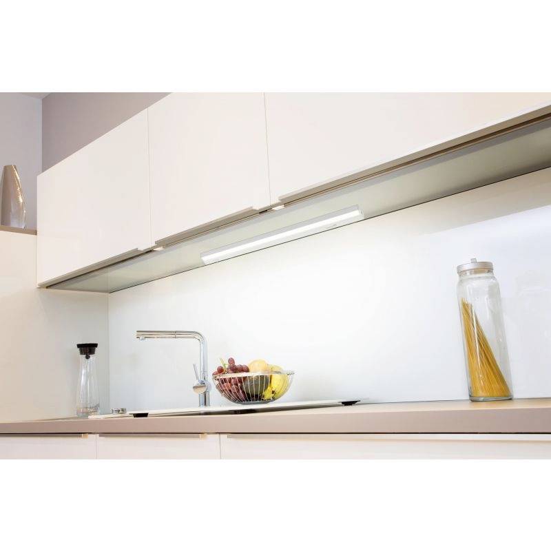 Schlicht gestaltete Küche mit weißem Schrank, beleuchtet durch eine Unterbauleuchte. Auf der Arbeitsplatte steht eine Obstschale und ein Glas mit Spaghetti.
