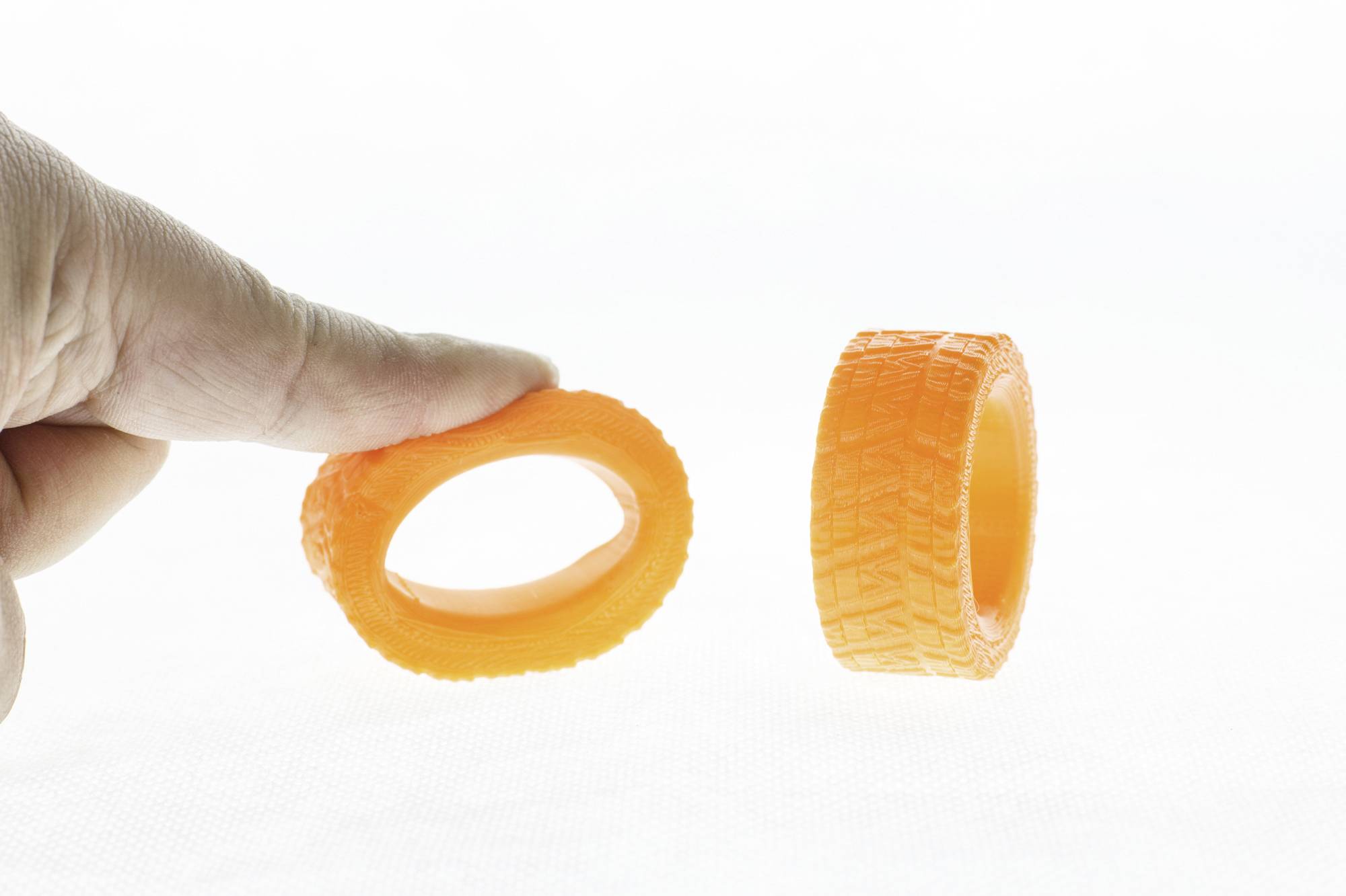 Eine Hand hält zwei orangefarbene, ringförmige Objekte. Eines steht aufrecht, während das andere zwischen Daumen und Finger gehalten wird.