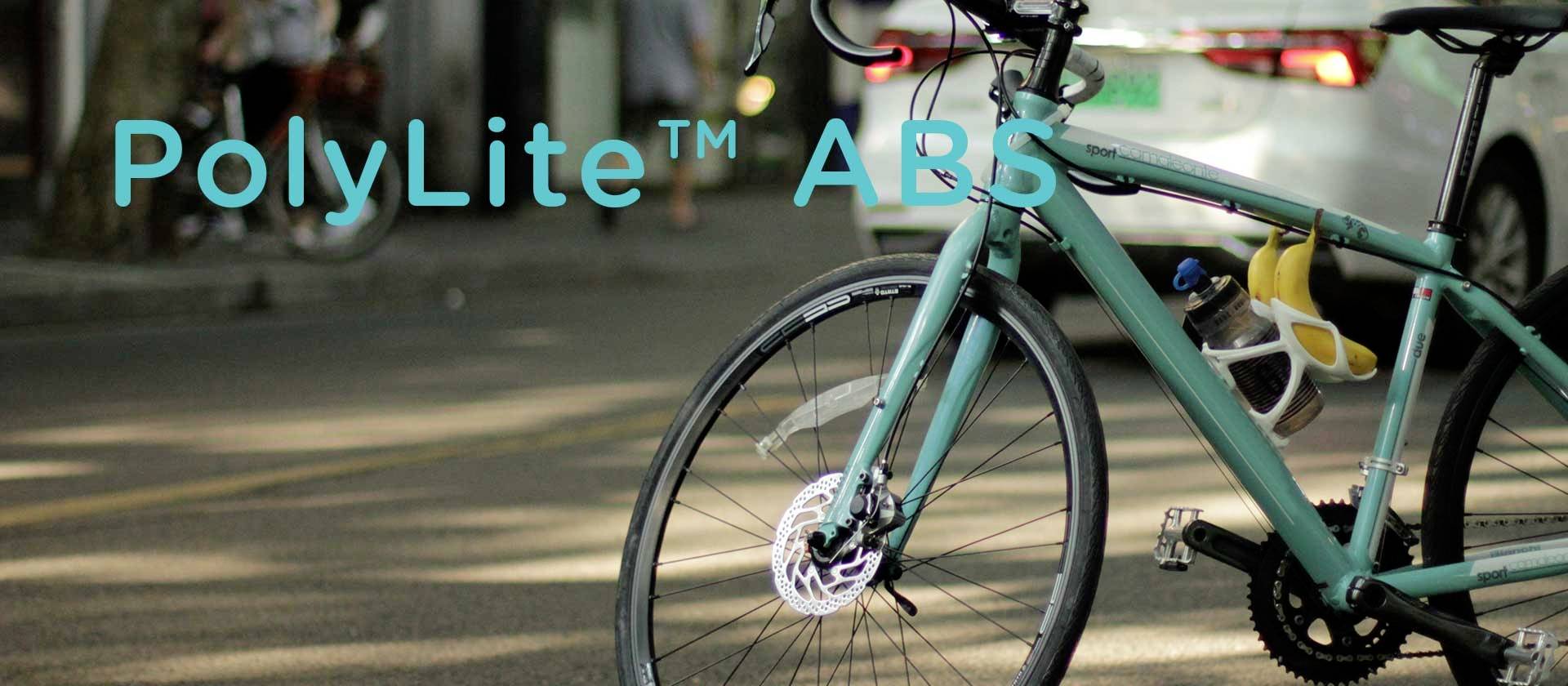Ein türkisfarbenes Fahrrad steht am Straßenrand mit einem Schriftzug 'PolyLite ABS' im Bildhintergrund. Autos sind im Hintergrund zu sehen.