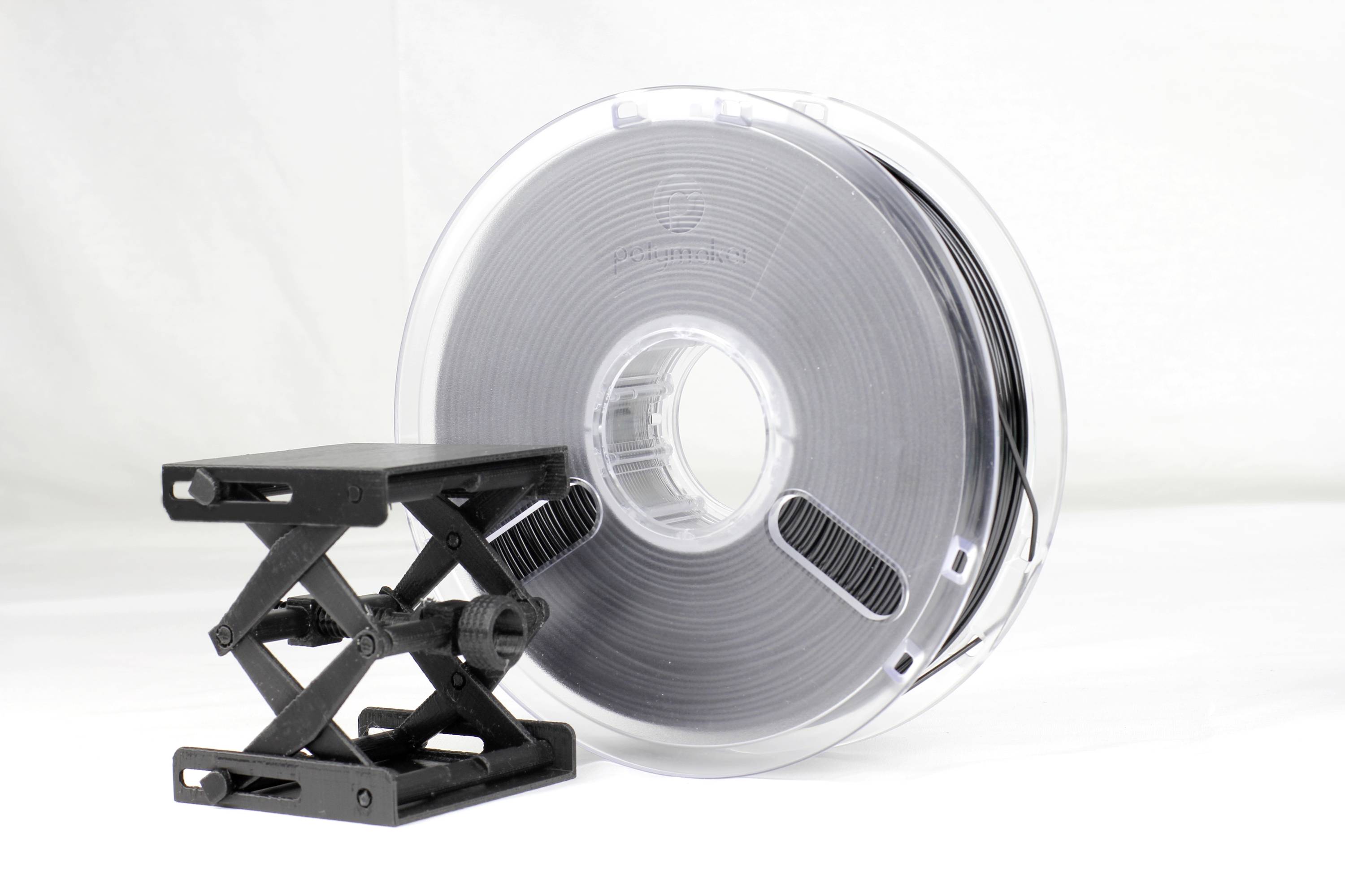 Ein schwarzes Filament für 3D-Drucker steht neben einem kleinen schwarzen Plattformheber gegen einen weißen Hintergrund.