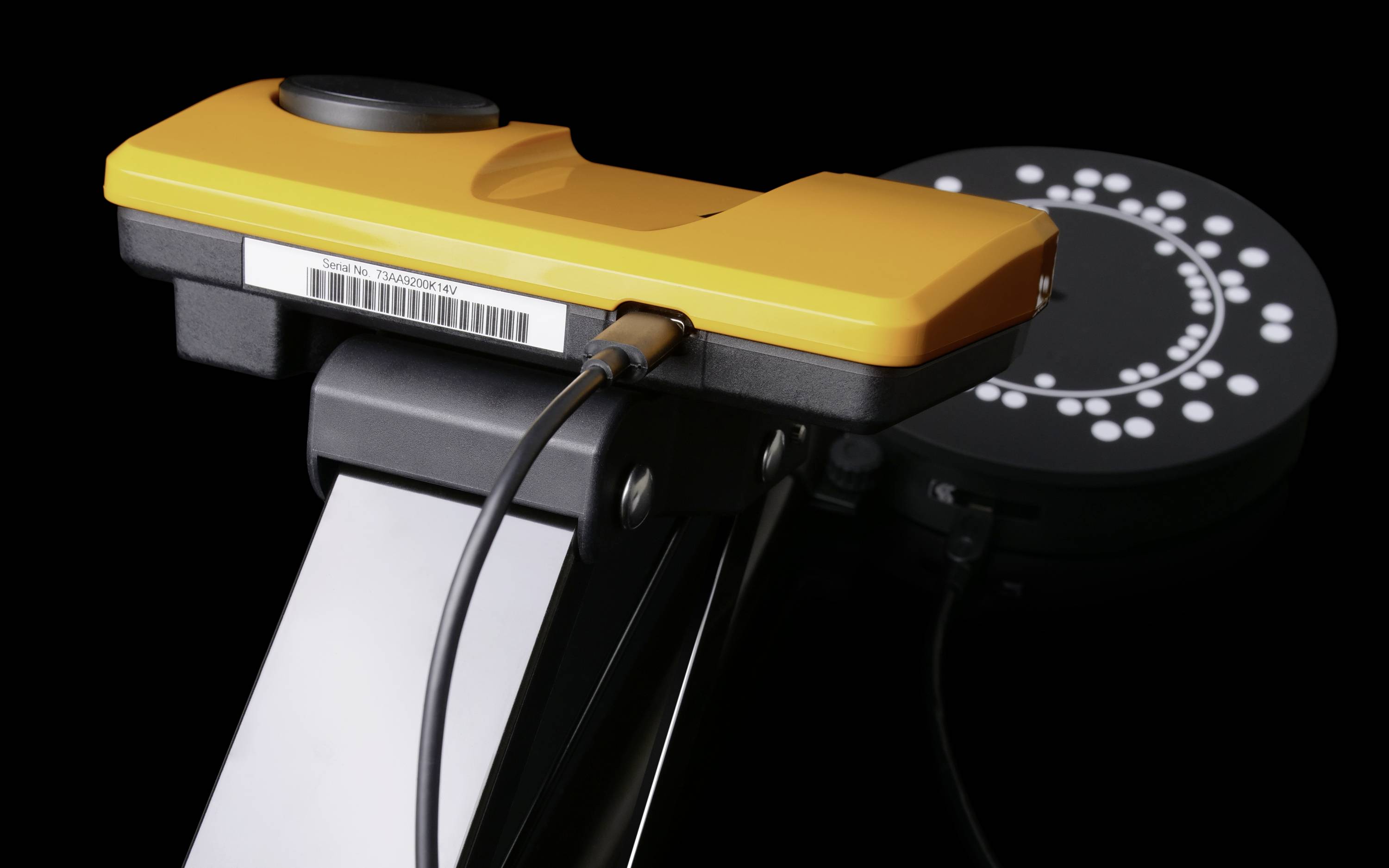 Ein Gelb-Schwarz-Gerät mit Kabelanschluss auf einem Stativ, vor einem schwarzen Hintergrund mit einem Punktmuster.