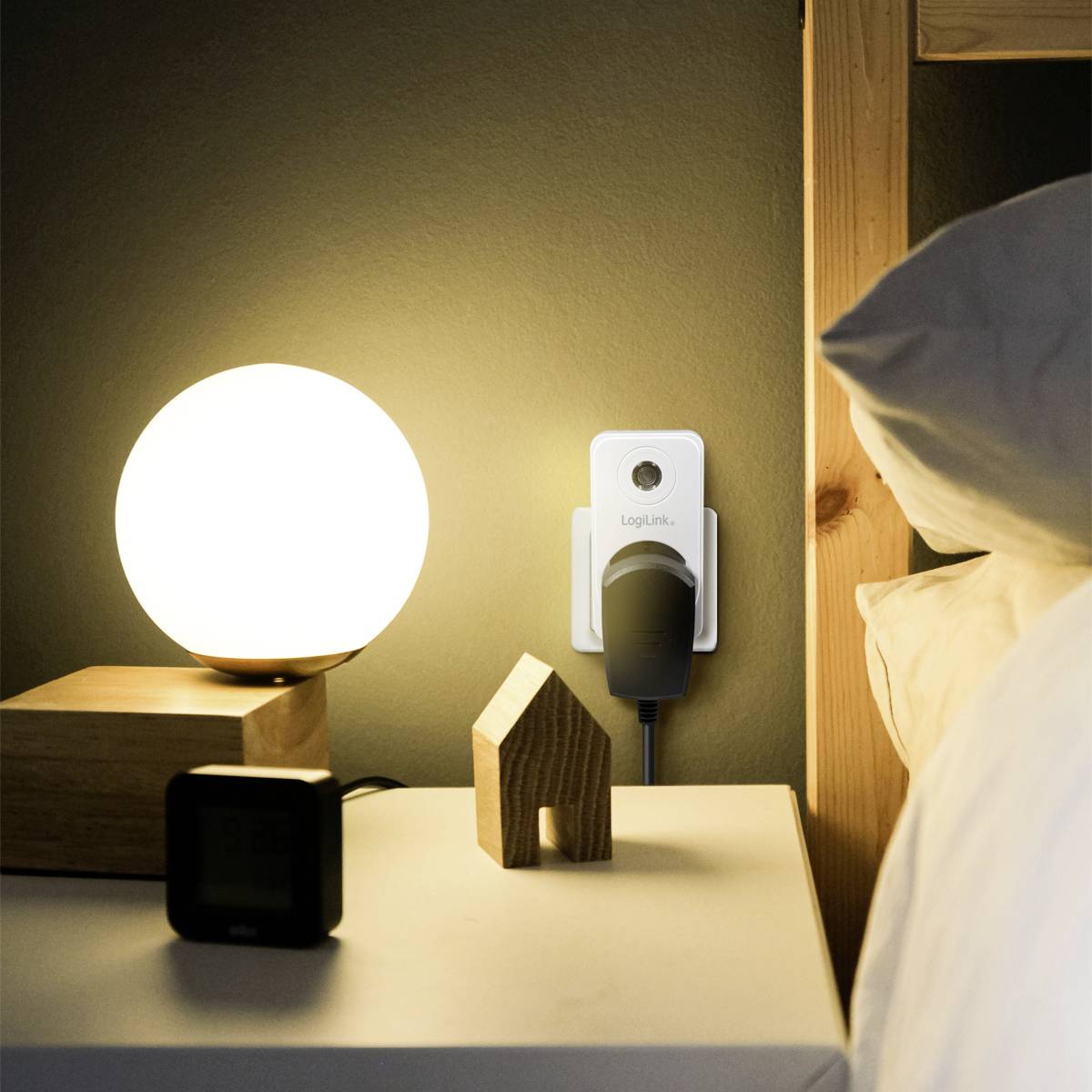 Nachttisch mit einer runden, leuchtenden Lampe, einer digitalen Uhr und einem Adapter, der in eine Steckdose an der Wand eingesteckt ist.