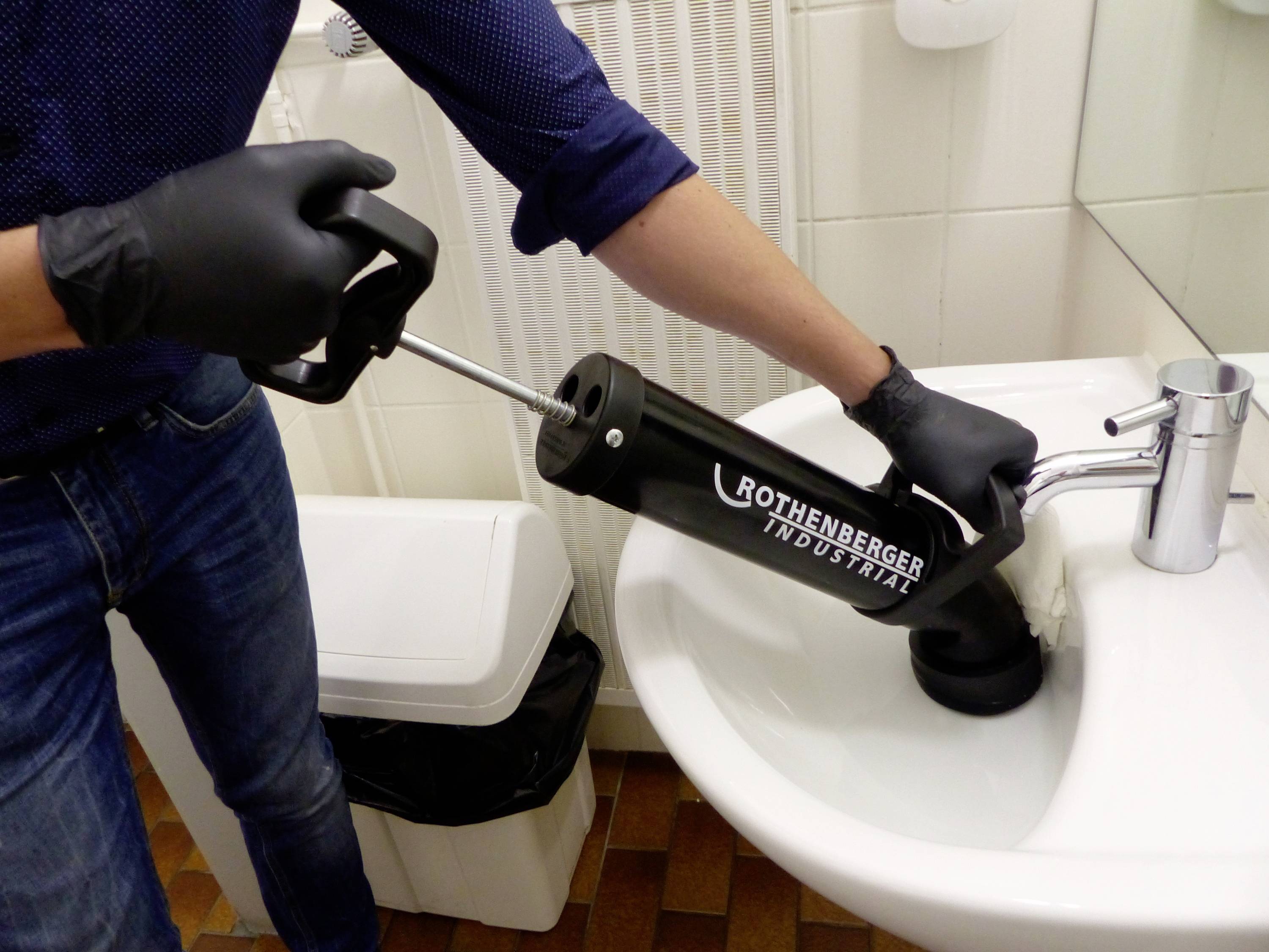 Eine Person in Handschuhen verwendet eine Abflussreinigungspumpe, um ein Waschbecken zu entstopfen.