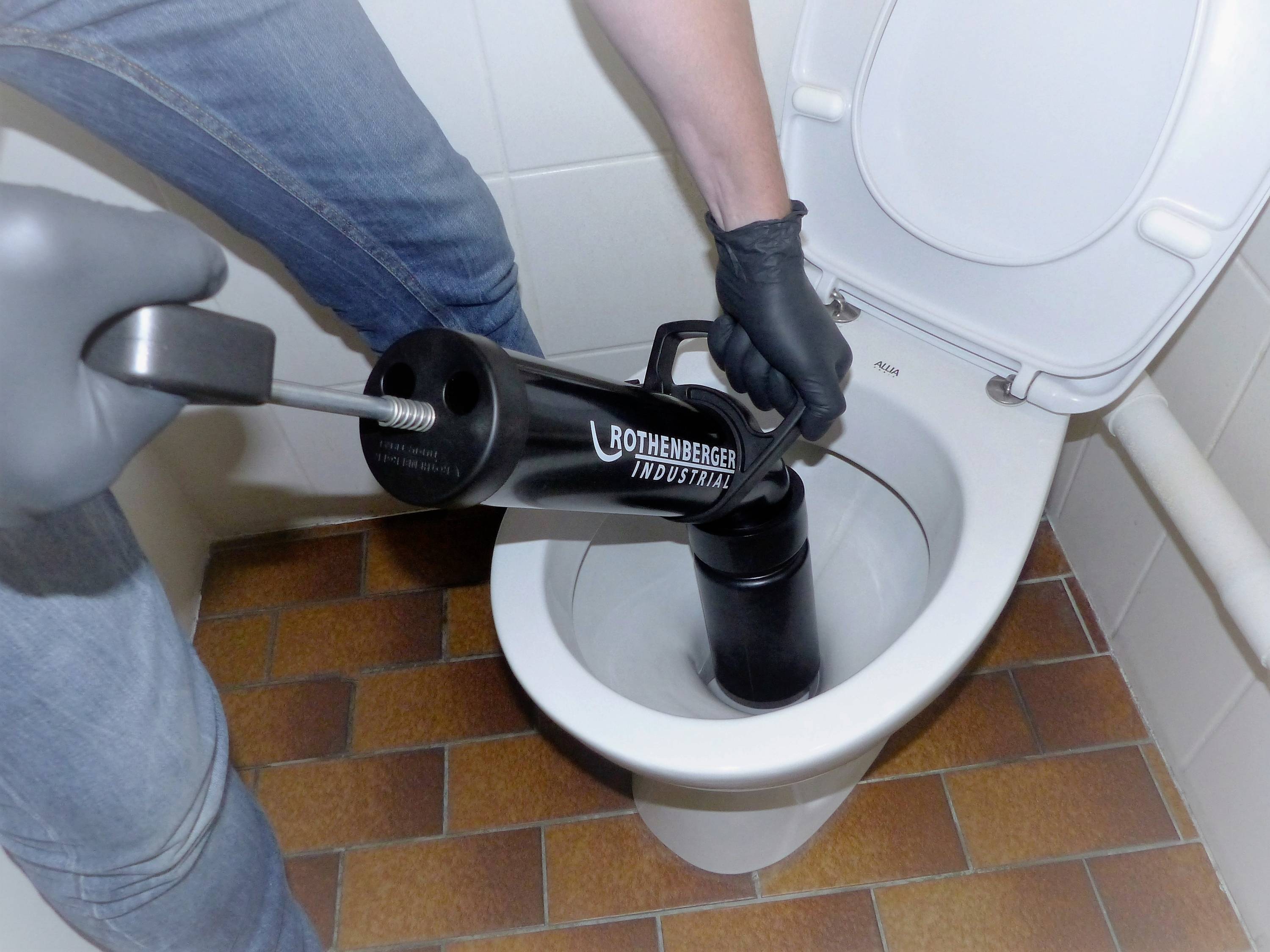Eine Person reinigt eine Toilette mit einem manuellen Abflussreiniger in einem Badezimmer.