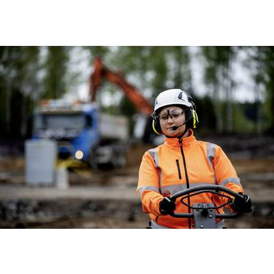 Eine Person in orangefarbener Schutzkleidung und Helm bedient schwere Maschinen auf einer Baustelle; im Hintergrund unscharf ein Lkw.