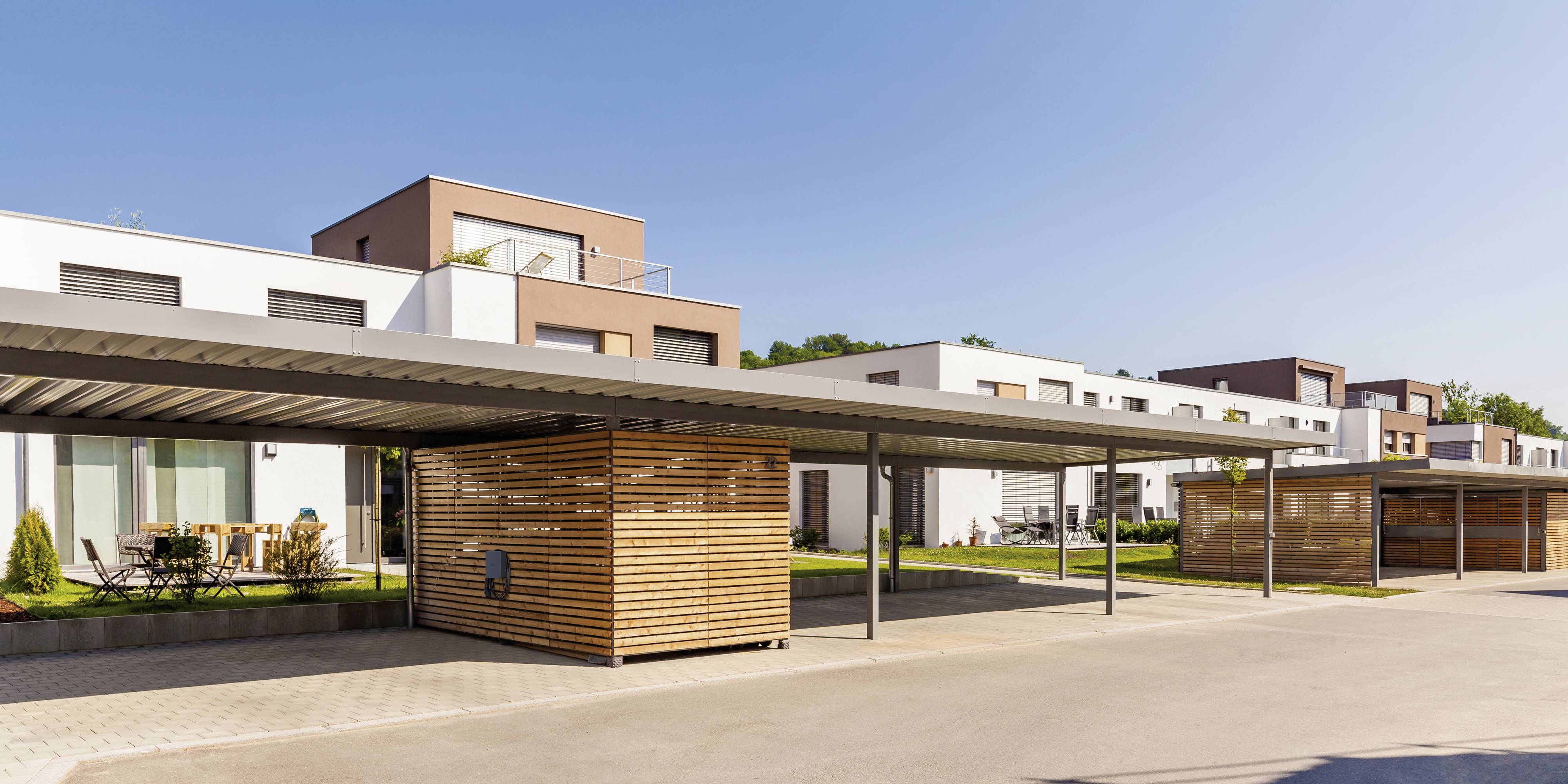Mehrfamilienhäuser mit moderner Architektur, weißen und braunen Fassaden, bepflanzten Balkonen und Holzelementen im Vordergrund.