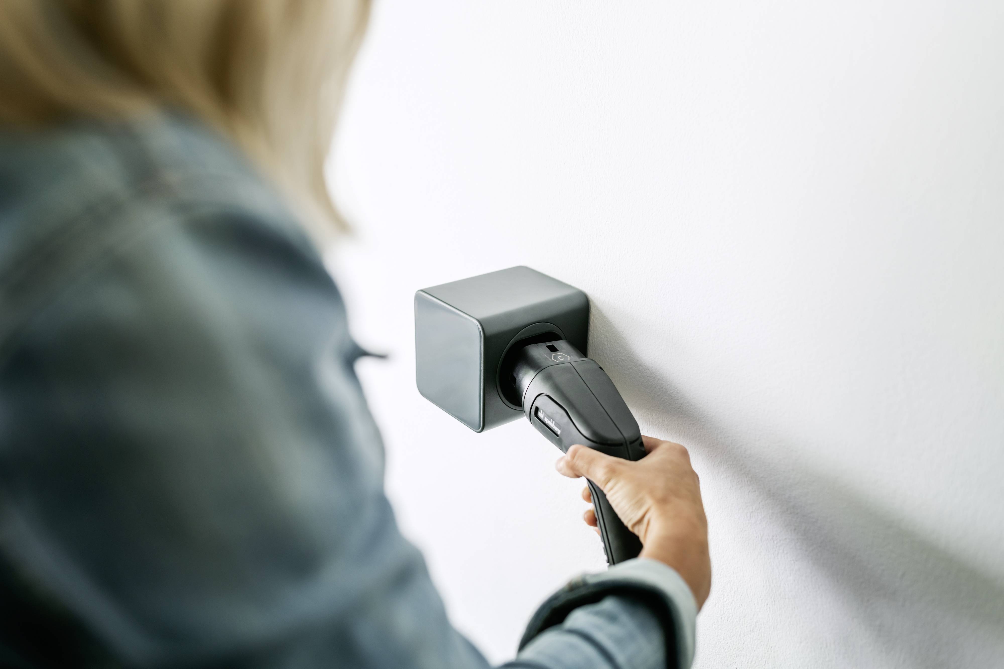 Eine Person steckt ein Ladekabel in eine Wandsteckdose. Fokussiert auf den Ladevorgang, möglicherweise für ein Elektrogerät.