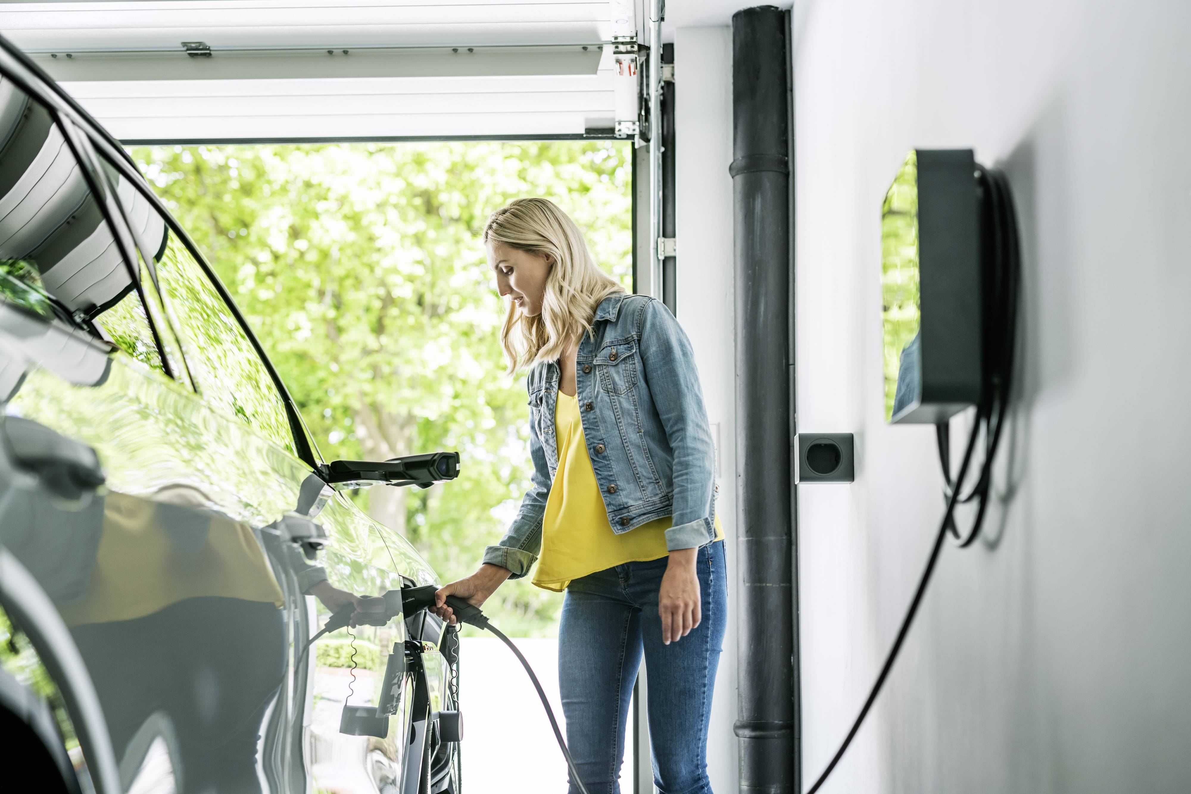 Eine Person lädt ein Elektroauto in einer Garage auf, indem sie ein Ladekabel an das Fahrzeug anschließt.