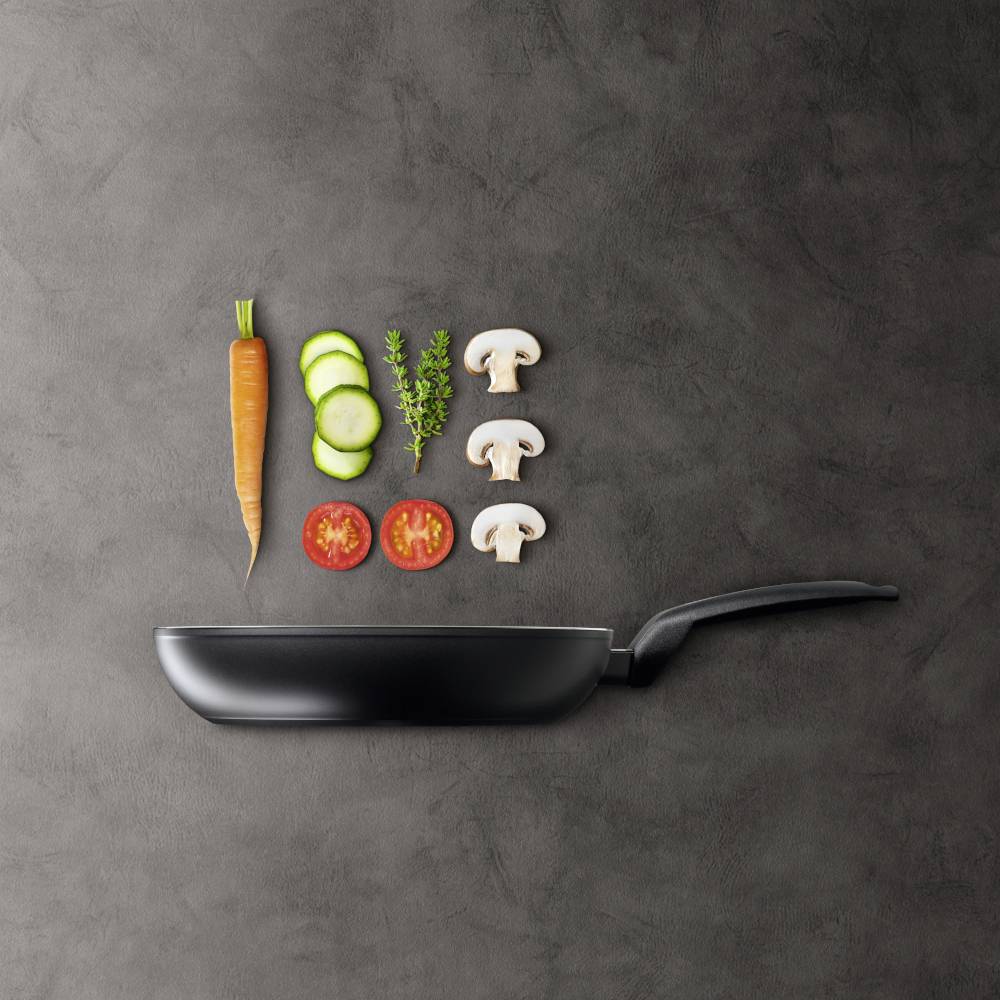 Pfanne mit gemischtem Gemüse darüber: Karotte, Zucchinischeiben, Tomaten, Champignons und Kräuter auf dunklem Hintergrund.